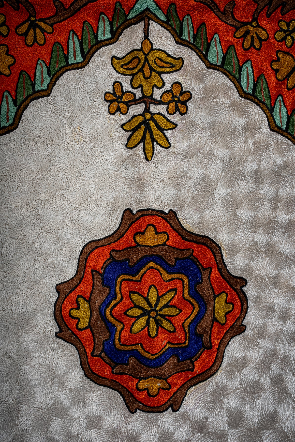 Close-up of the prayer mat's orange, blue and gold floral medallion on an ivory ground