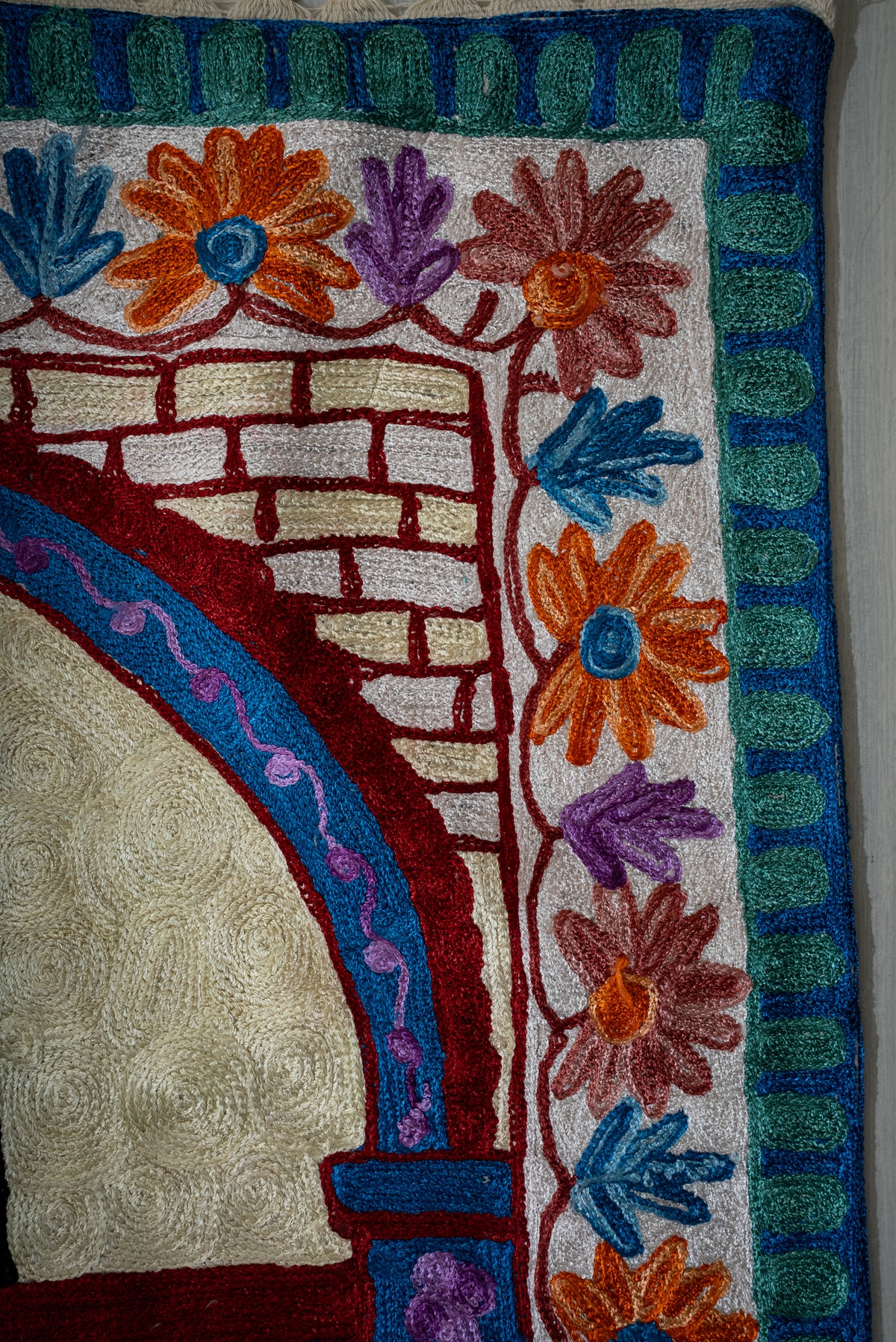 Upper corner of the prayer mat showing orange and purple flowers beside a burgundy brick pattern and blue arch