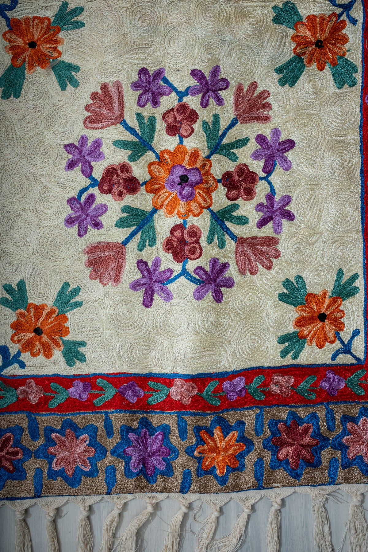 Lower section of the ivory prayer mat with a floral circle, orange corner flowers, patterned borders and cream tassels