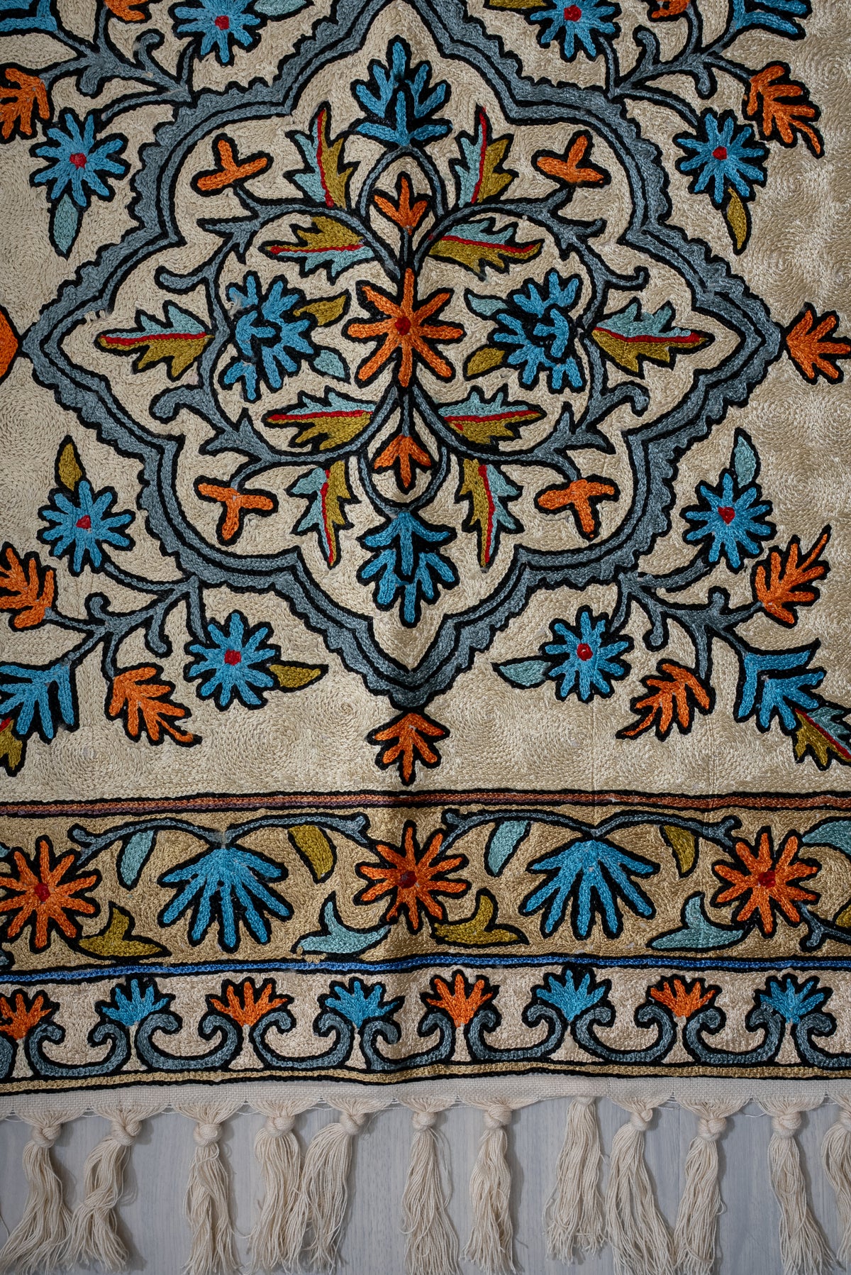 Prayer mat's blue and orange floral medallion above layered floral borders and cream tassels