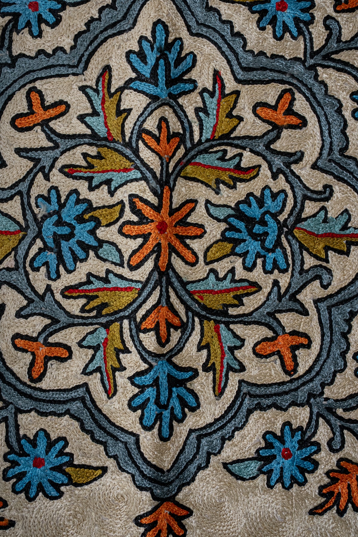 Close-up of the prayer mat's symmetrical blue and orange floral medallion outlined in dark thread
