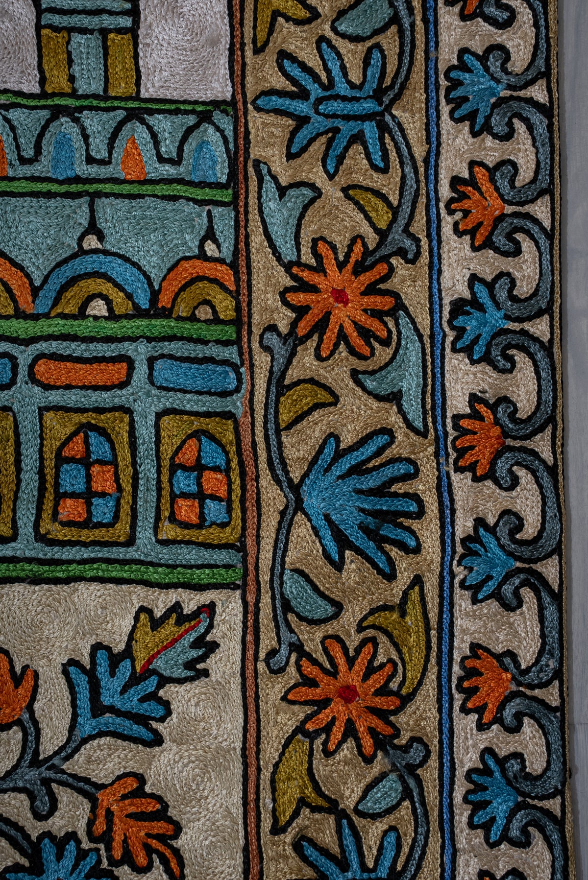 Close-up of blue and orange embroidered flowers along the prayer mat's layered side borders