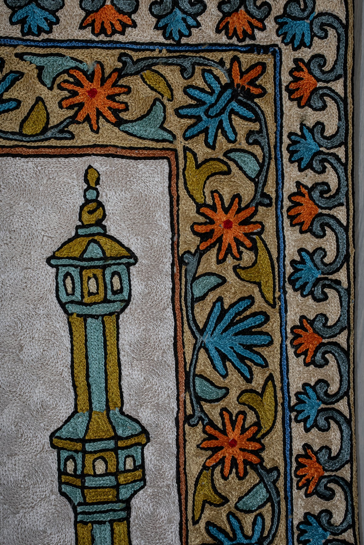 Prayer mat corner showing a slender minaret beside blue and orange floral borders