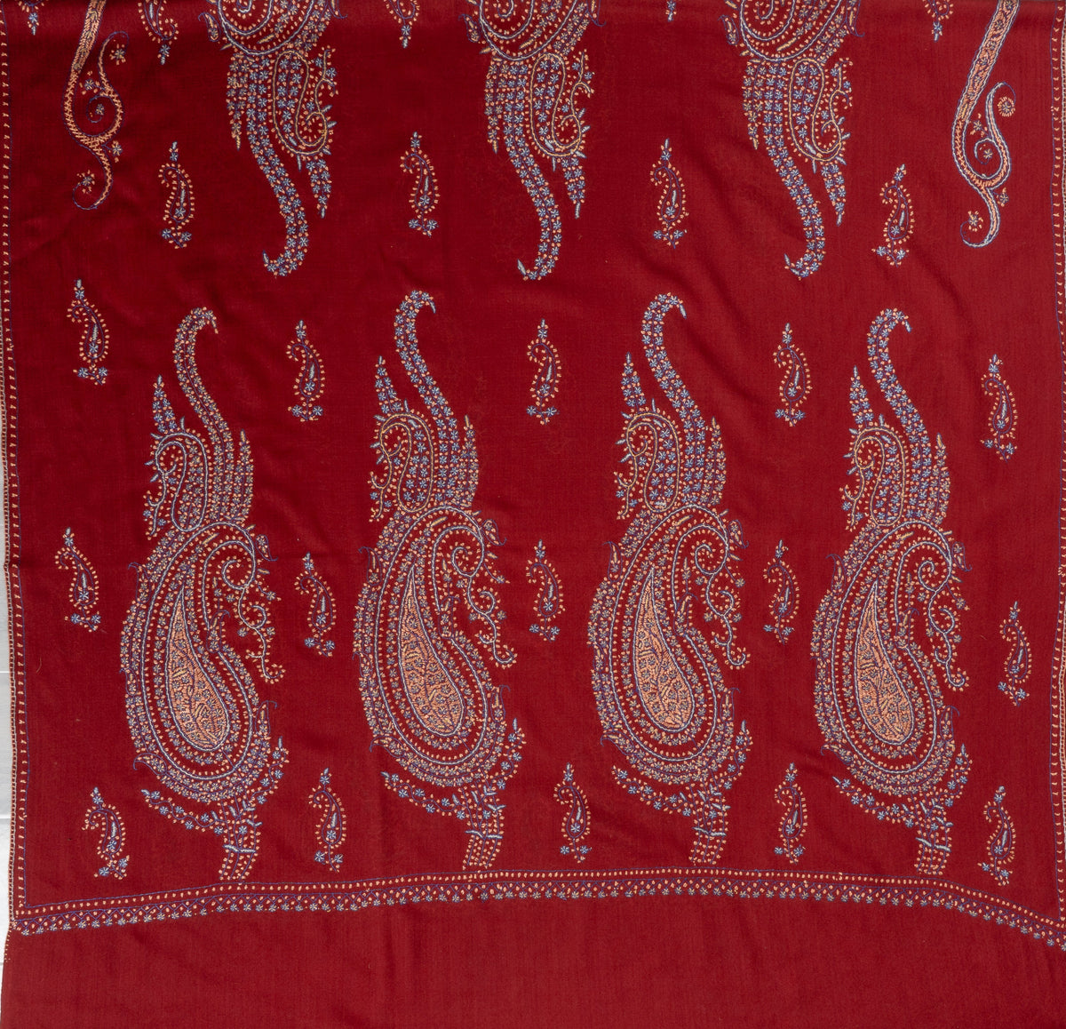 Deep red shawl laid flat with alternating large and small multicoloured Sozni paisleys above a plain end