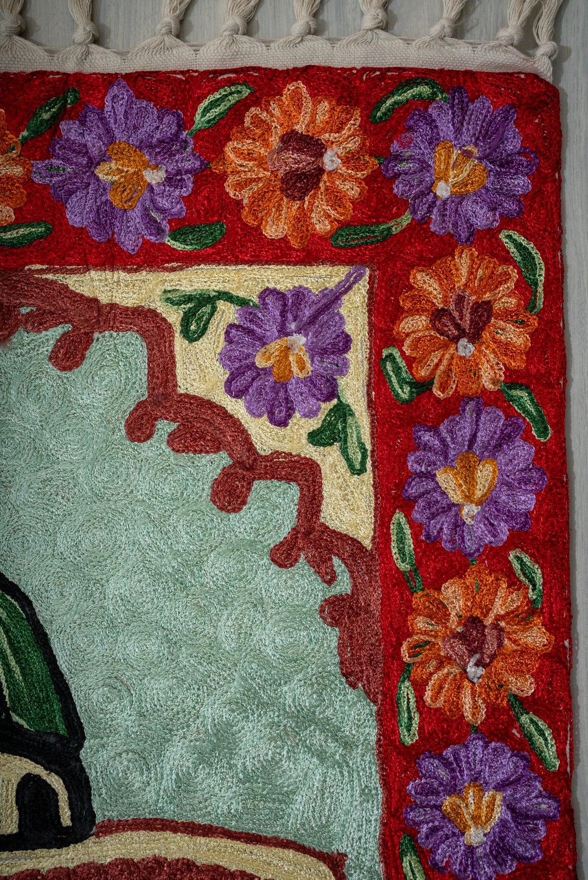 Upper corner of the prayer mat with a purple and orange floral border beside a burgundy-edged arch
