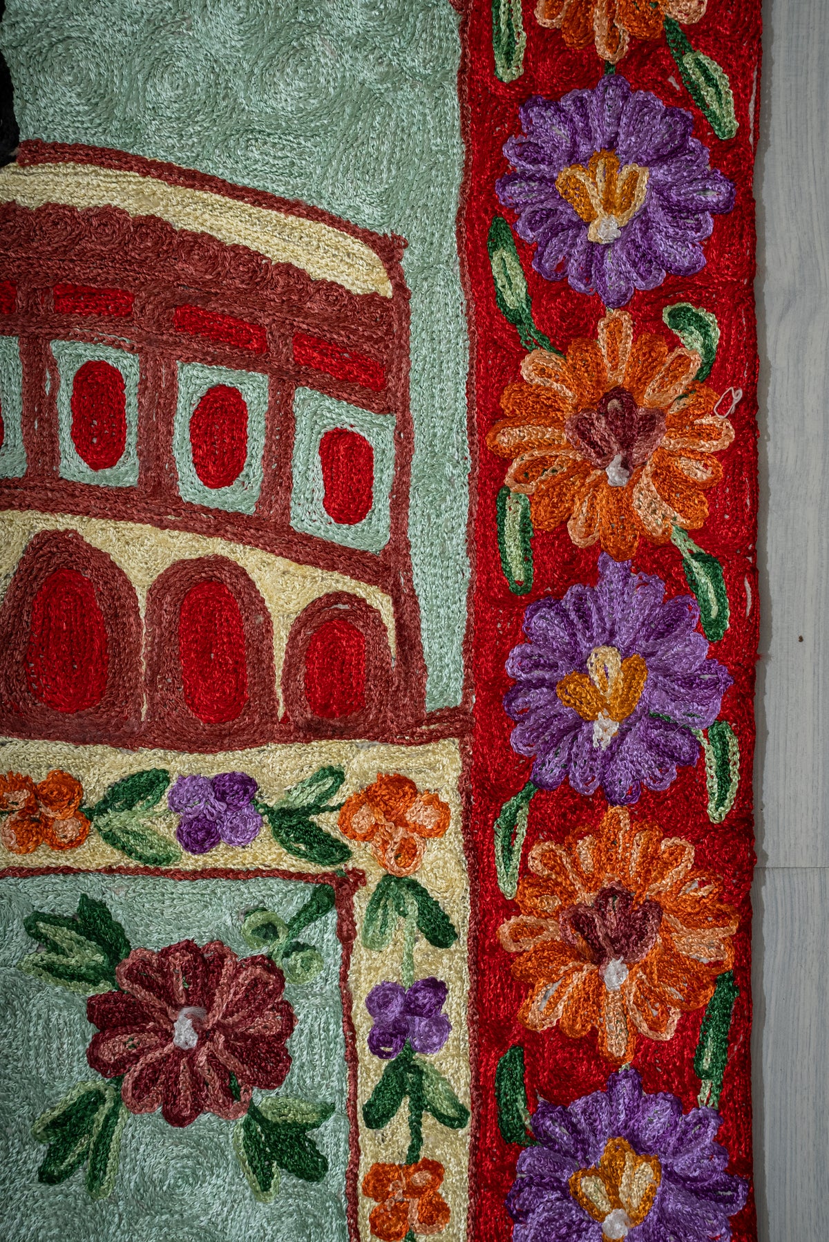 Side detail of the prayer mat with purple and orange flowers on a red border beside the architectural motif
