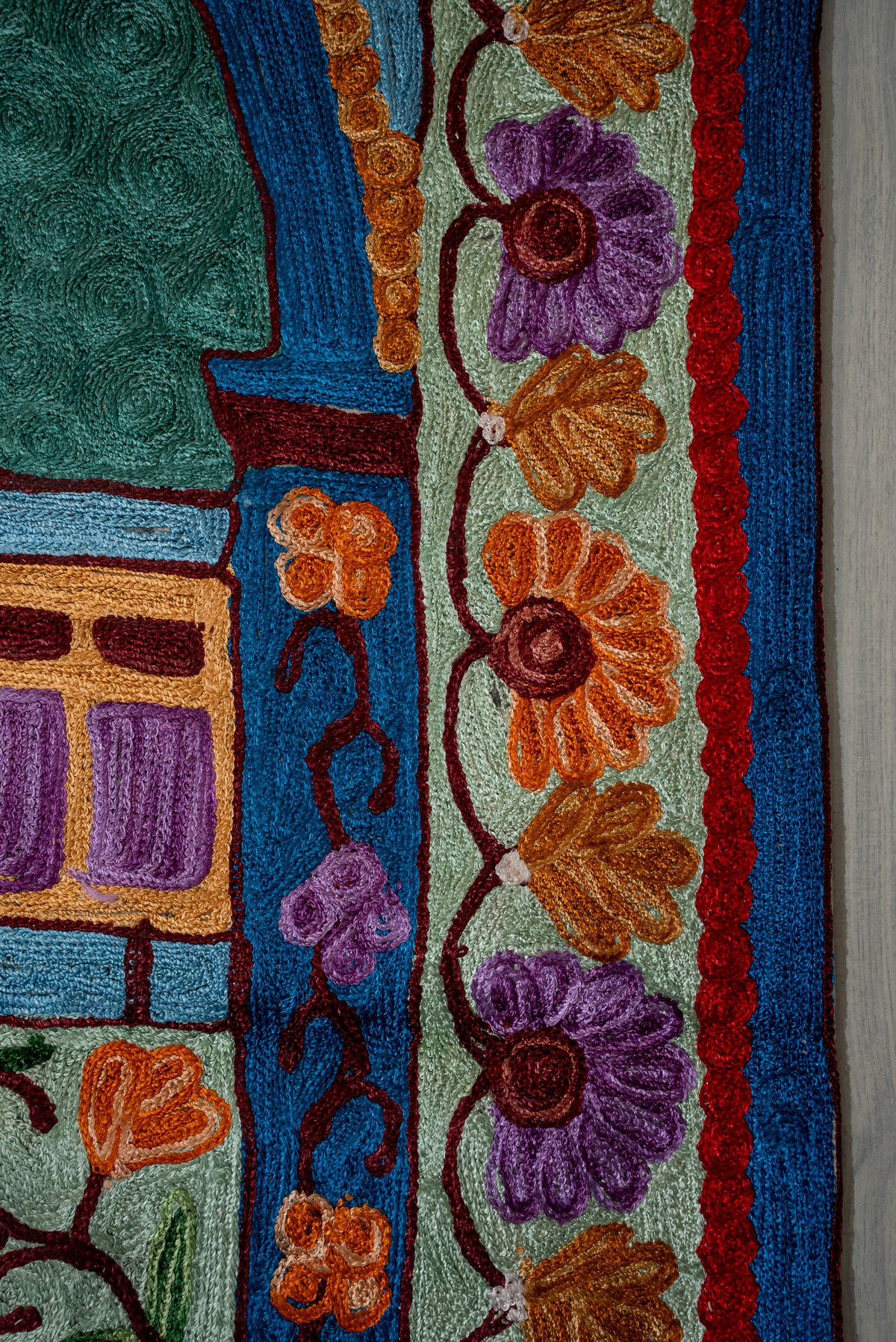 Close-up of orange and purple embroidered flowers along the pale green border of a teal prayer mat