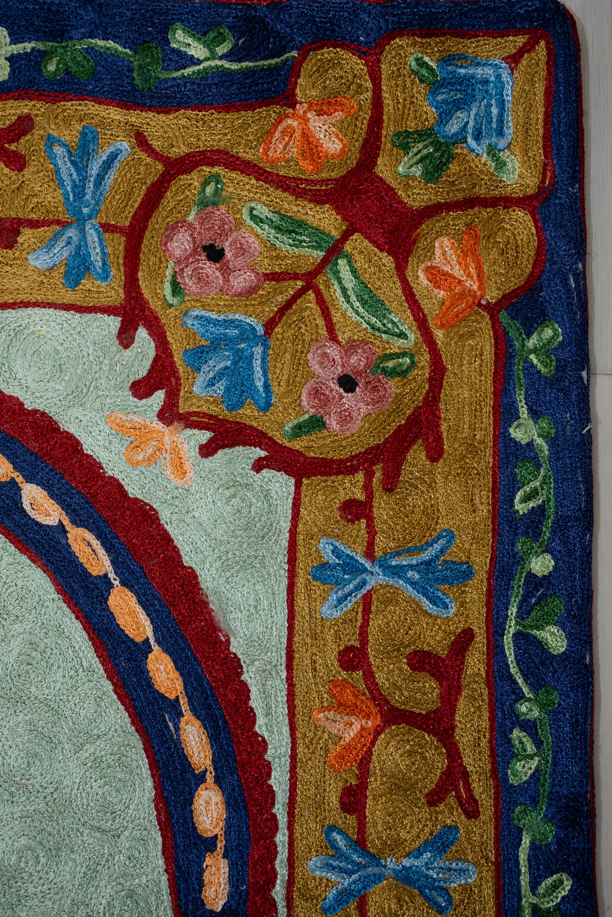 Upper corner of the prayer mat showing pink and blue flowers on gold beside a navy and red arch