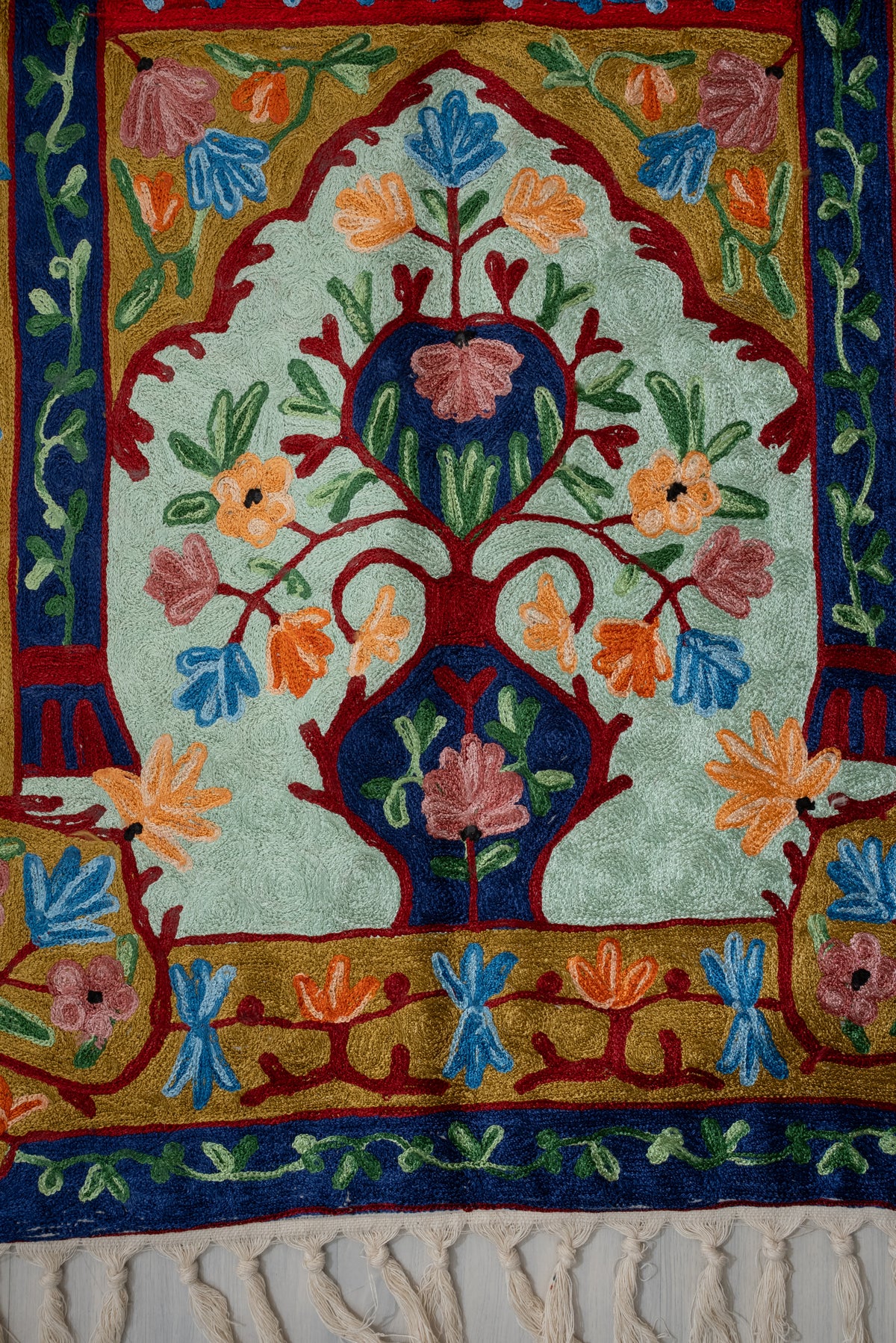 Lower end of the prayer mat with navy vase motifs, multicoloured flowers, gold borders and cream tassels