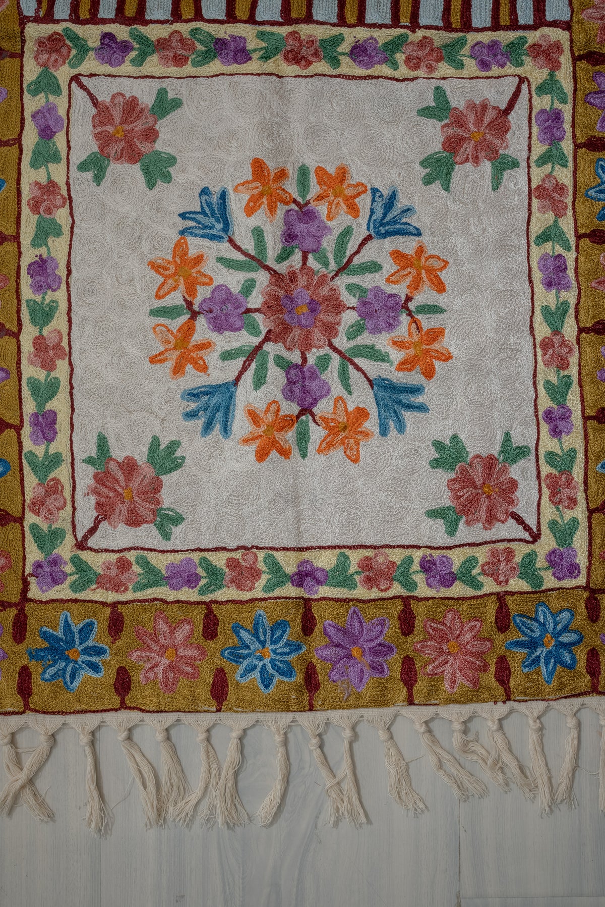 Lower section of a prayer mat with a multicoloured floral medallion on cream, ochre flower borders and cream tassels