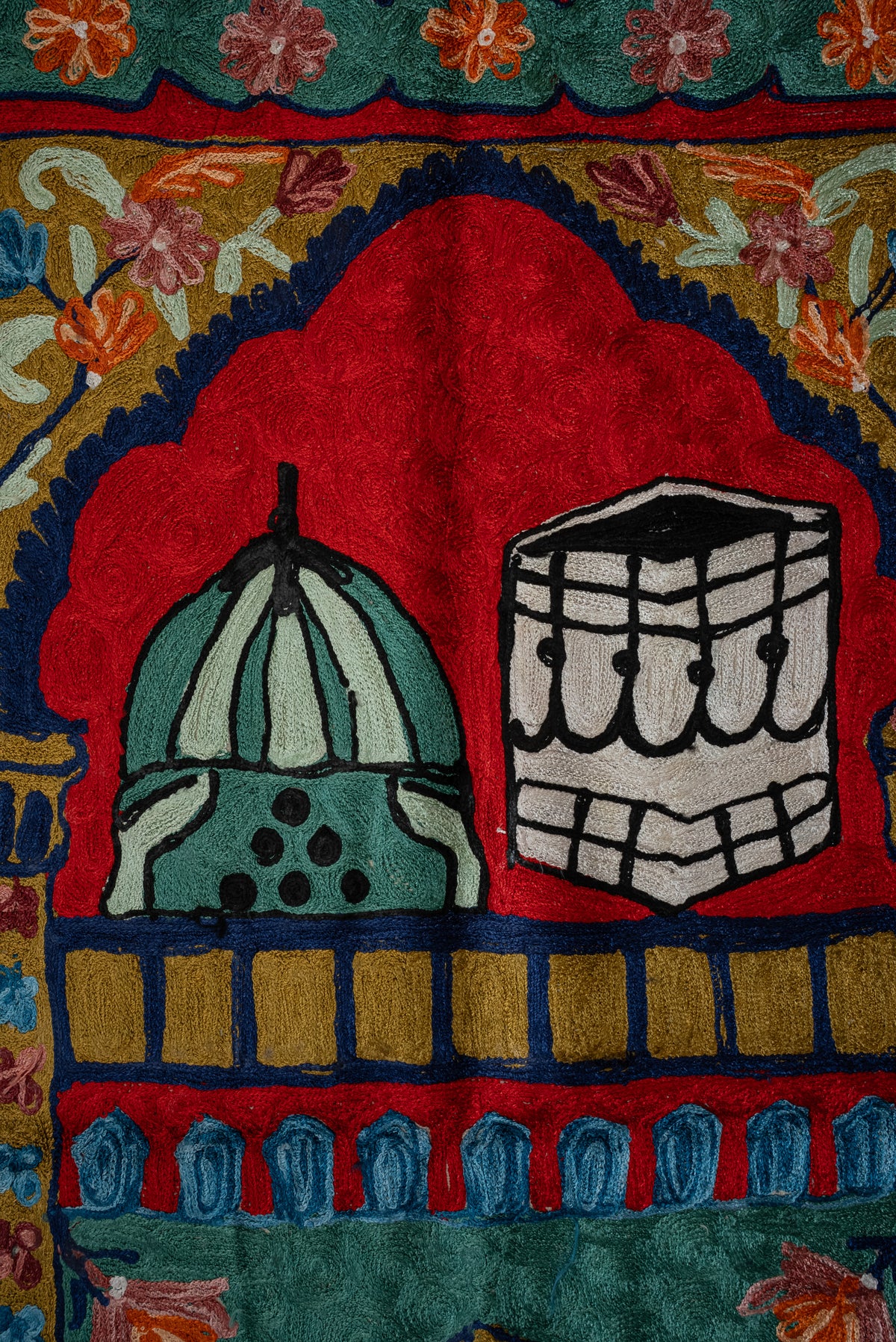 Green dome beside a black-and-white Kaaba motif beneath a red arch on the embroidered prayer mat