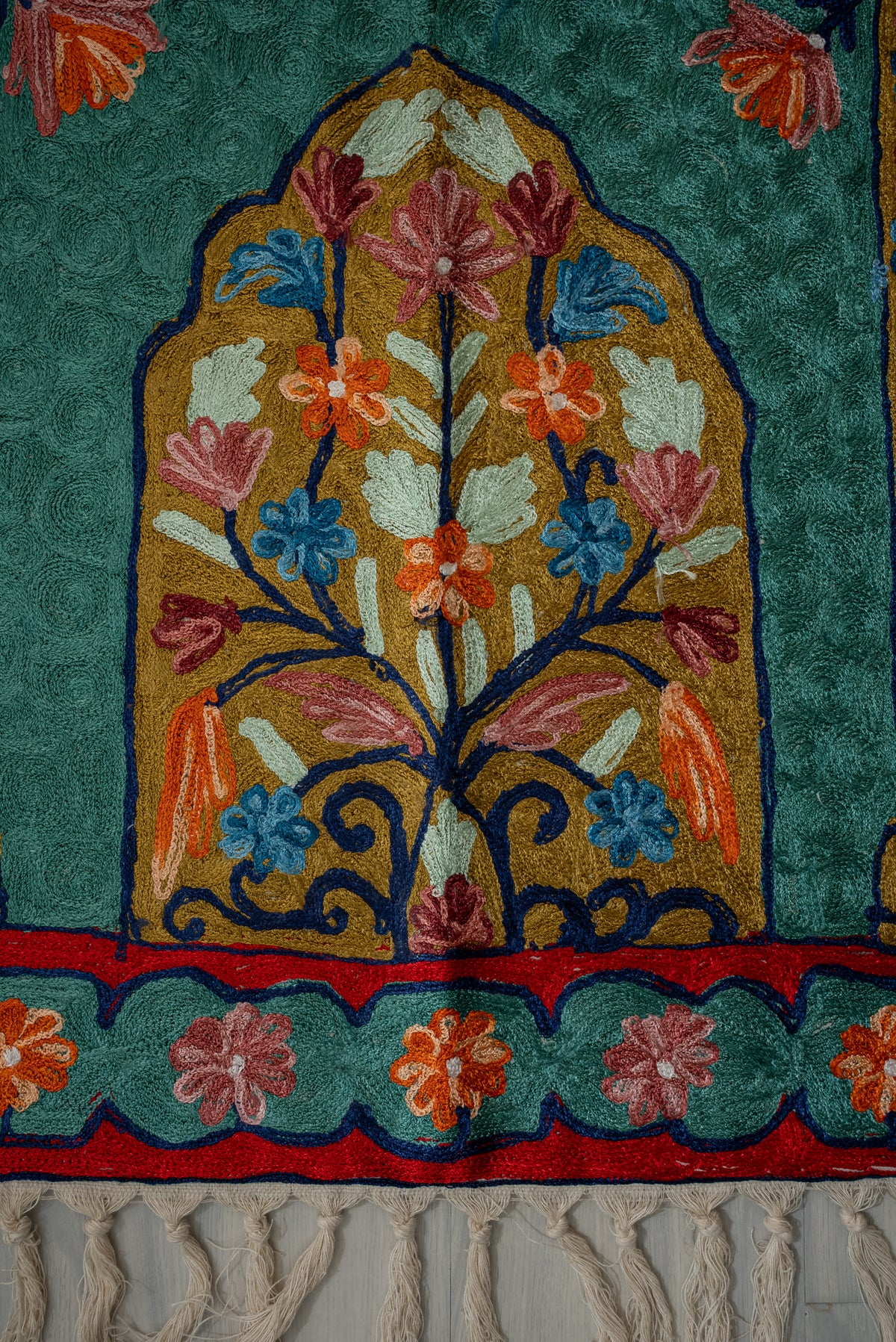 Colourful embroidered floral tree inside a gold arch, above teal flower borders and cream tassels