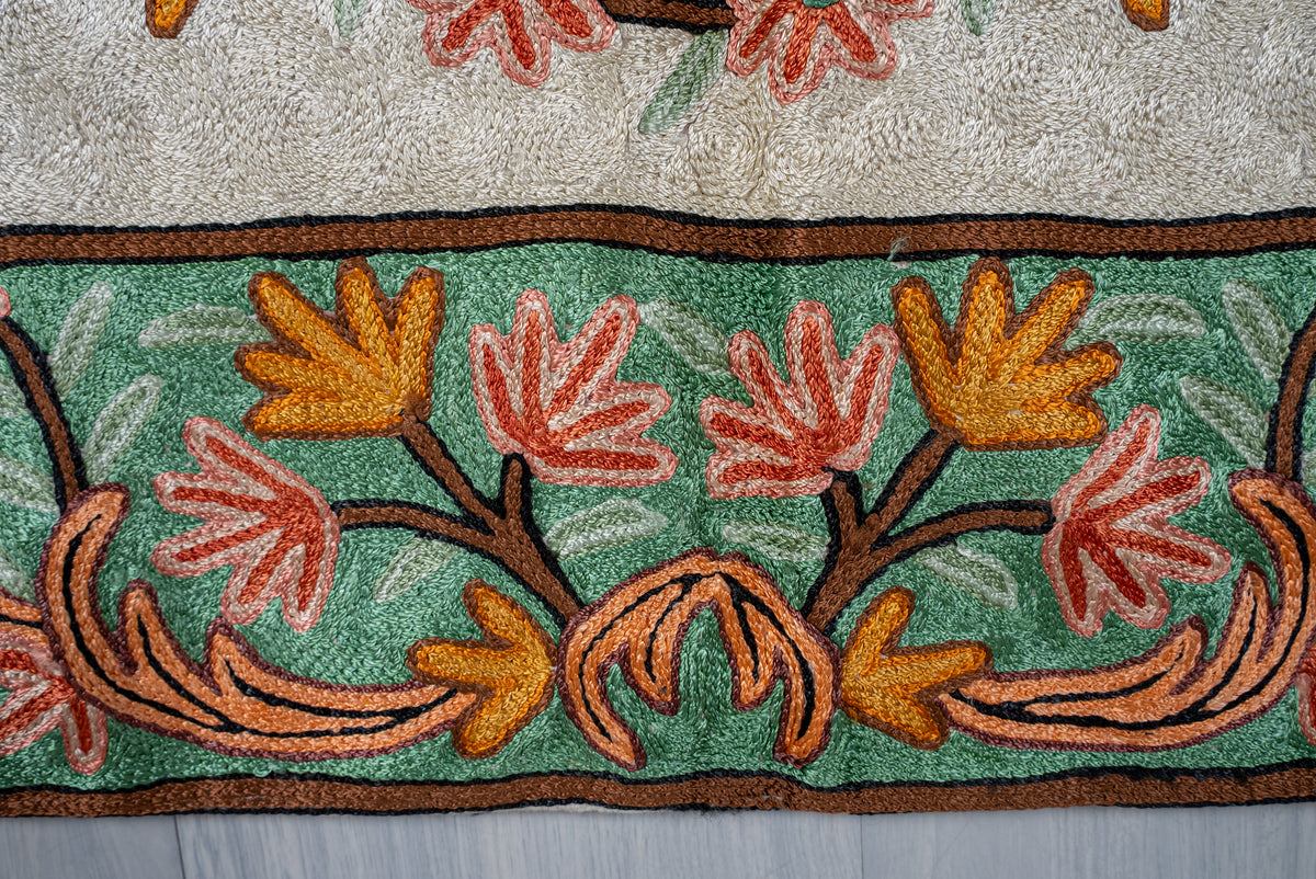 Green border of an Aari chain-stitch rug embroidered with coral flowers, golden leaves and peach scrolls