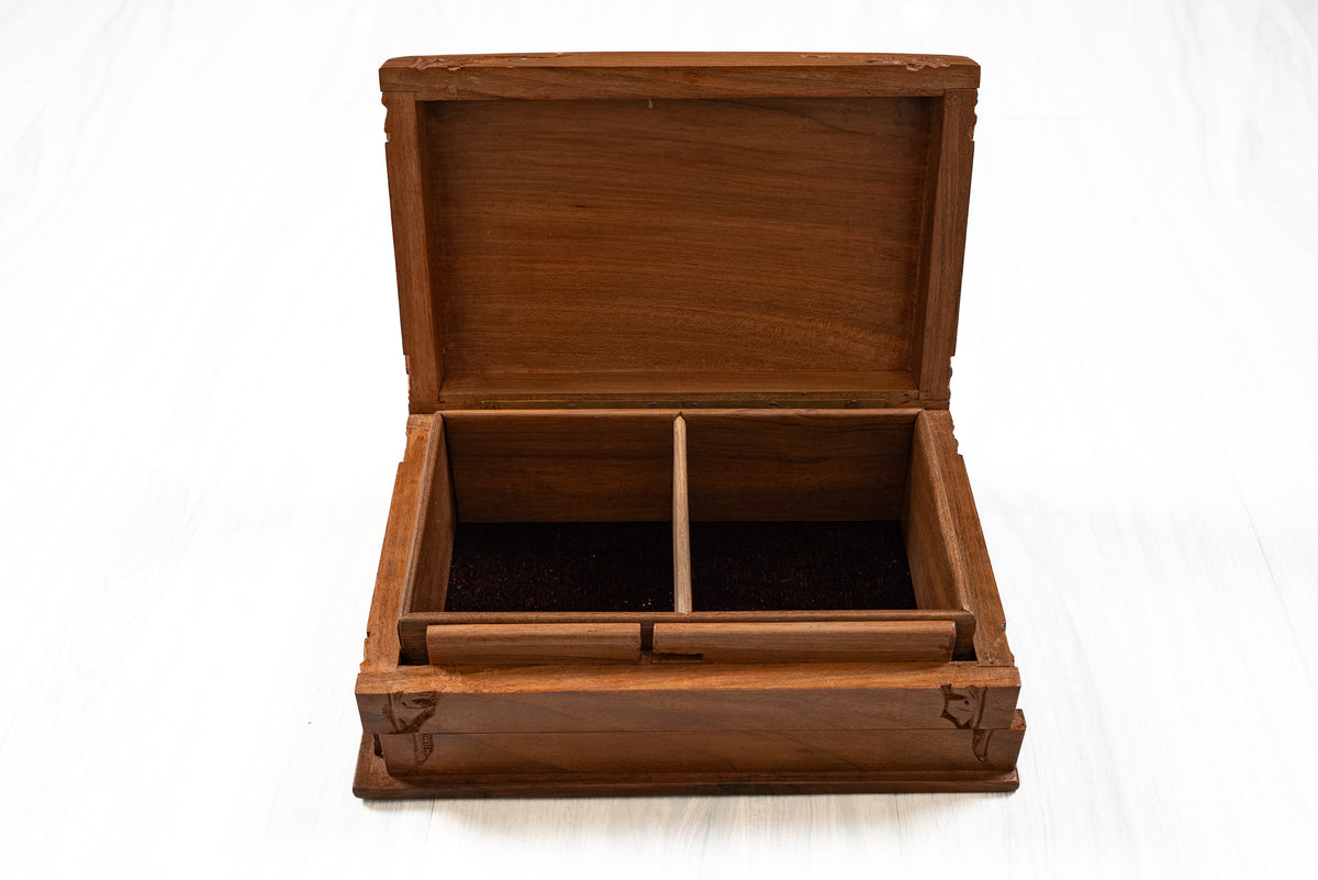 Front view of an open walnut wood box with a central divider, two dark-lined compartments and carved corner details