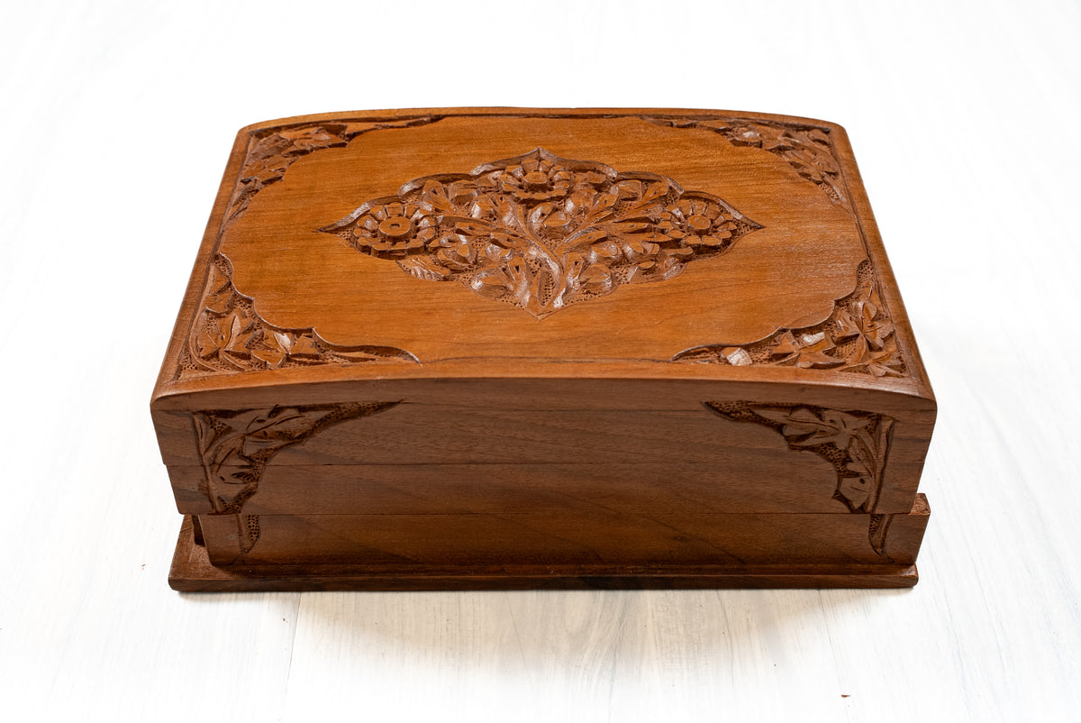 Front view of a closed walnut wood box with a floral medallion on the lid and carved leaves at the corners