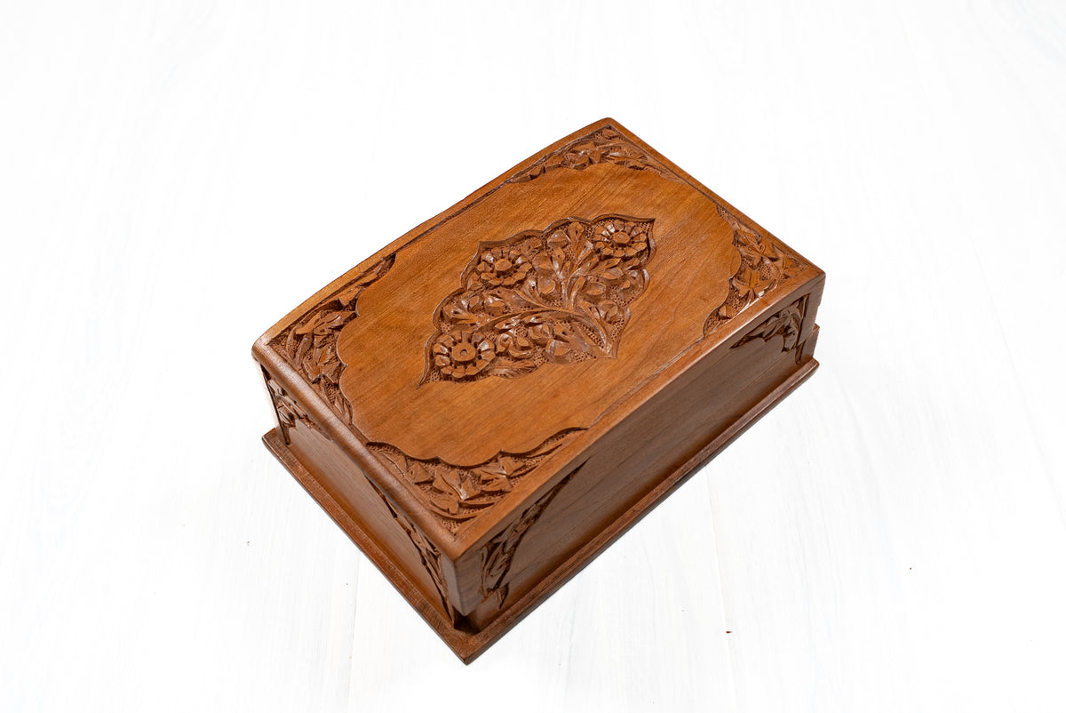 Closed walnut wood box viewed diagonally from above, showing the floral lid medallion and carved corners