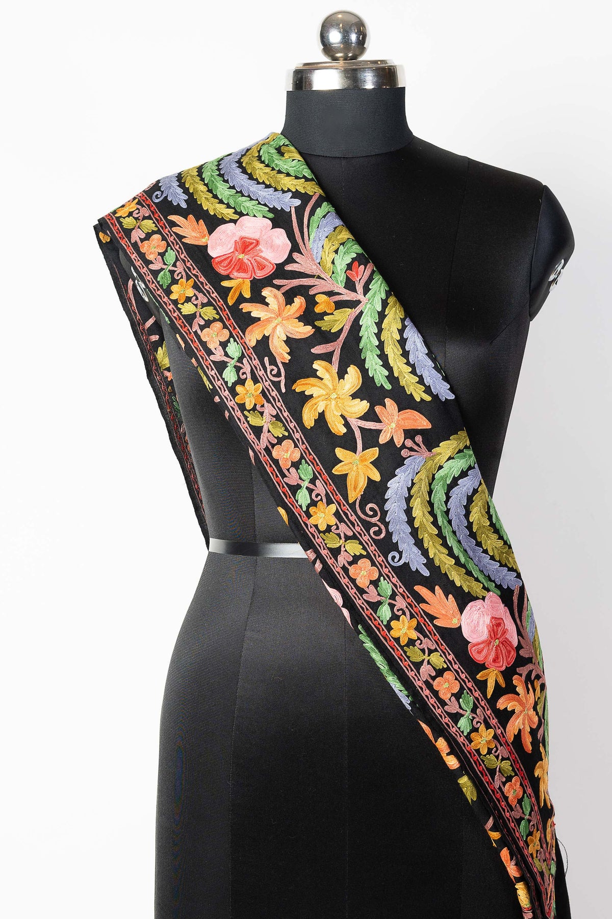Black stole folded into a narrow diagonal drape on a mannequin, highlighting its colourful floral border.
