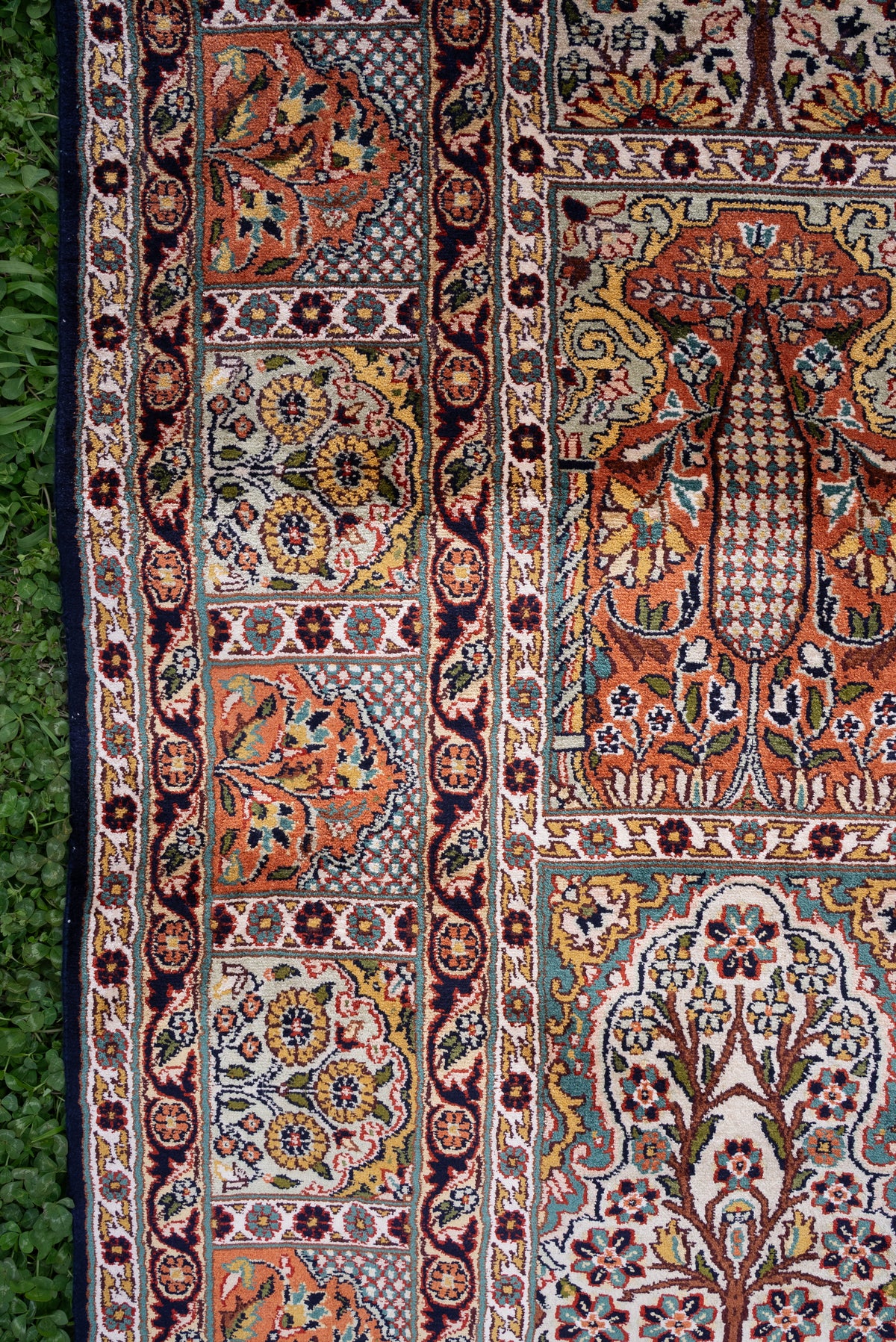 Side detail of a silk carpet with framed cypress-like trees and flowering plants beside a narrow floral border