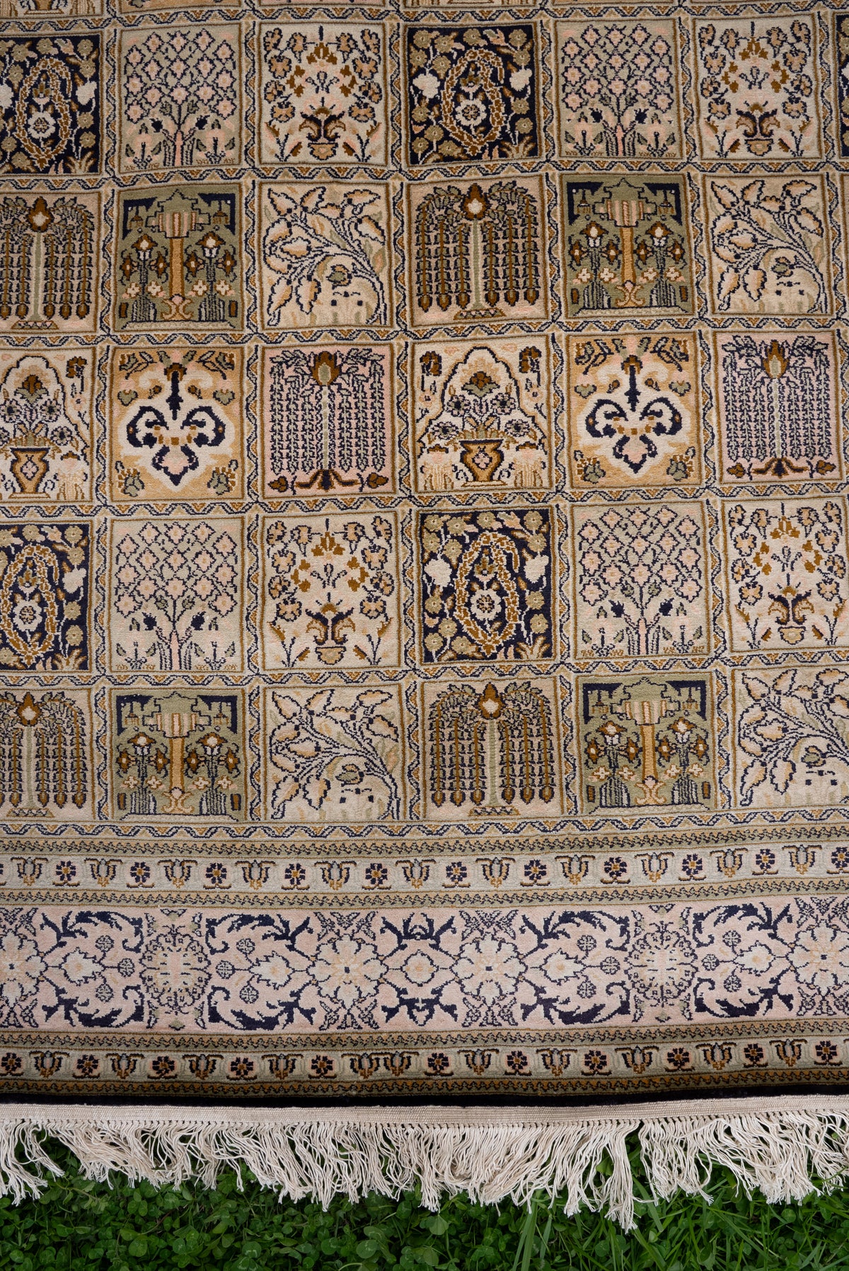 Lower section of the ivory silk carpet, showing patterned grid panels, navy floral border and pale fringe