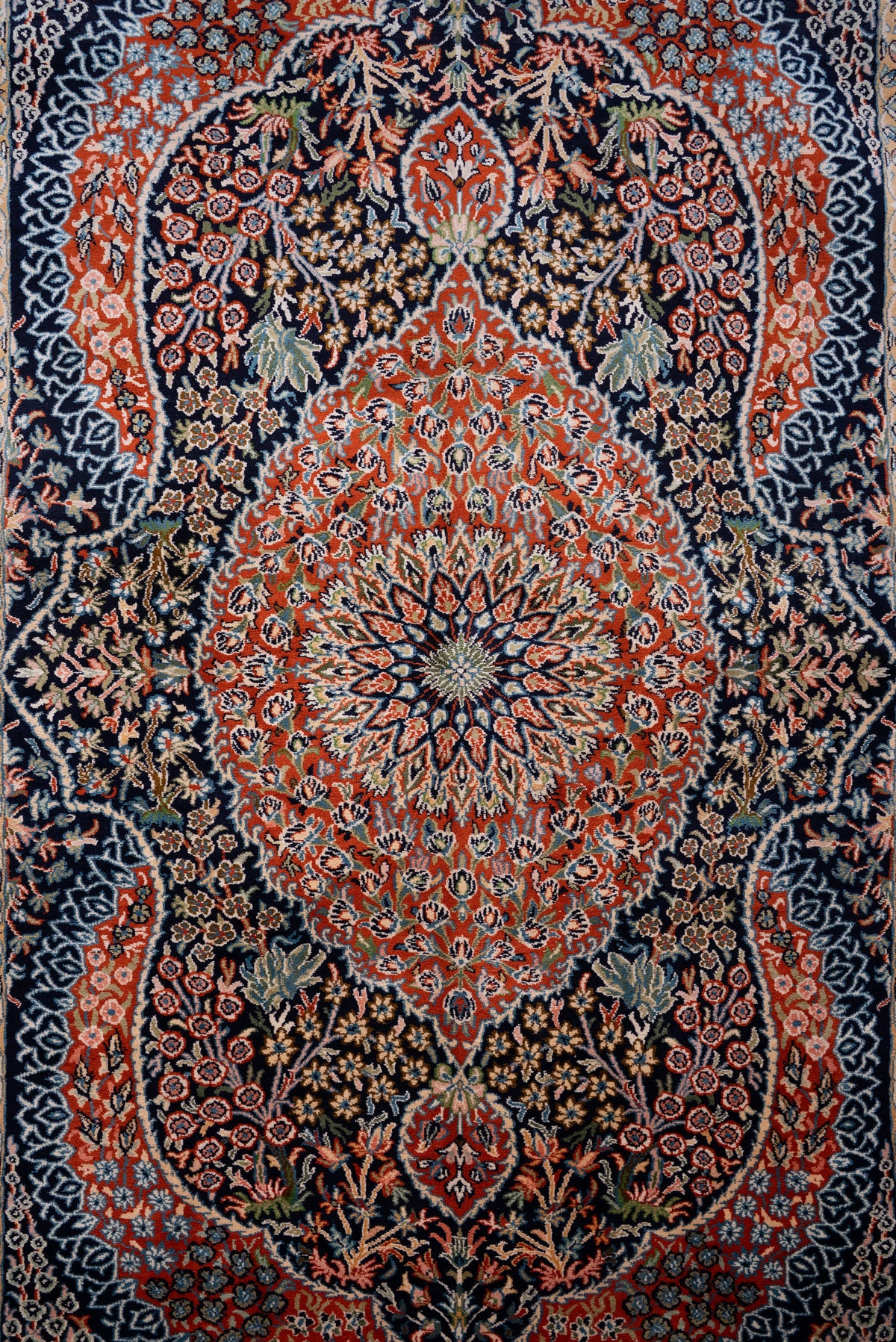 Lengthwise detail of the silk carpet's red central medallion and floral vines on a dark ground