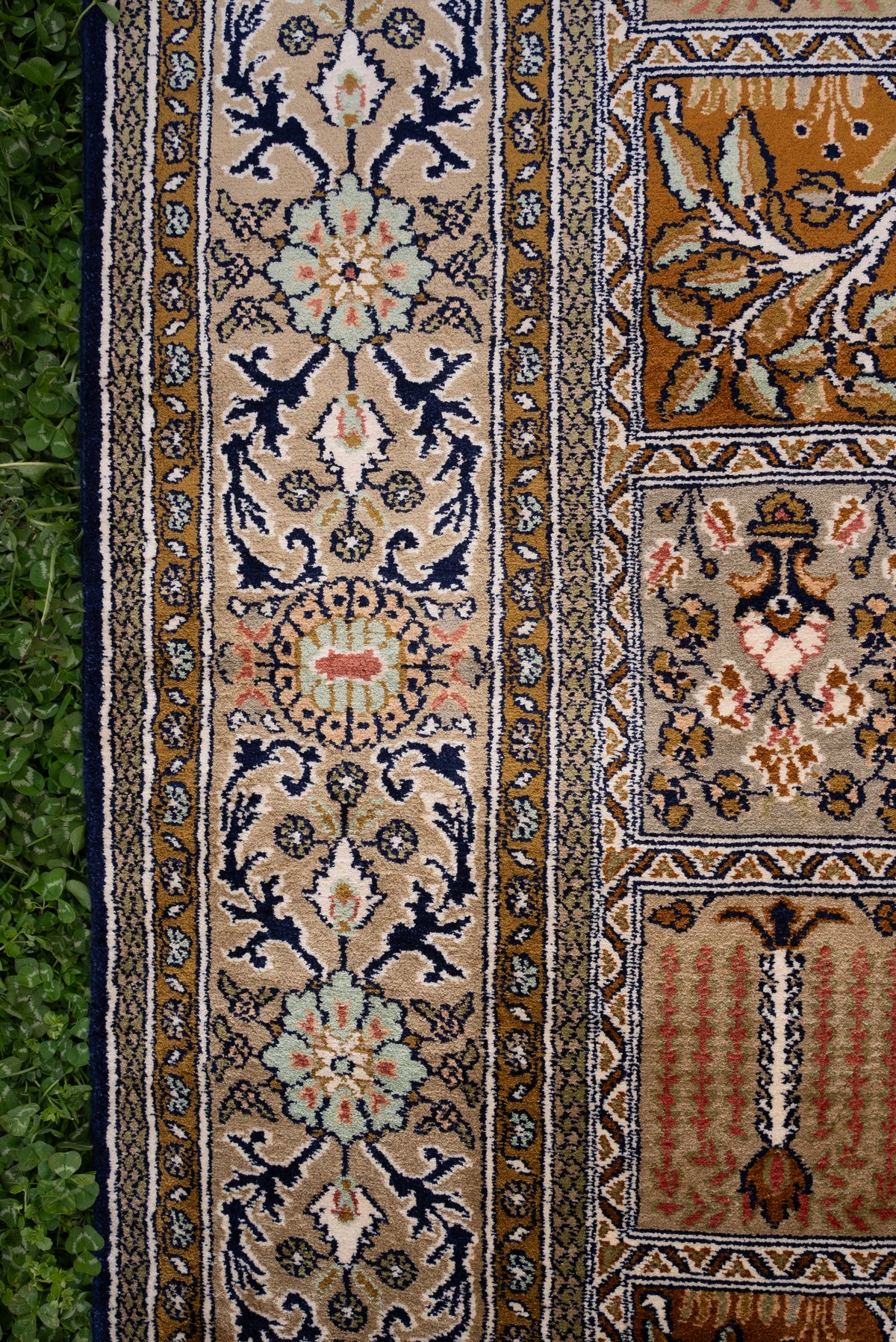 Side border of a silk carpet with navy floral vines on ivory beside gold and ivory ornamental panels