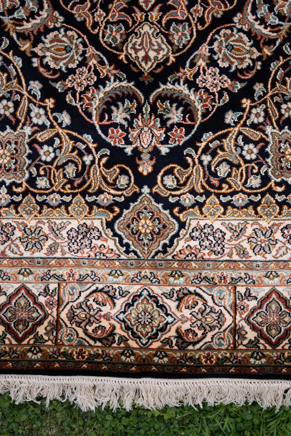 Lower section of a dark mulberry silk carpet with curling floral vines, cream and rust borders and ivory fringe