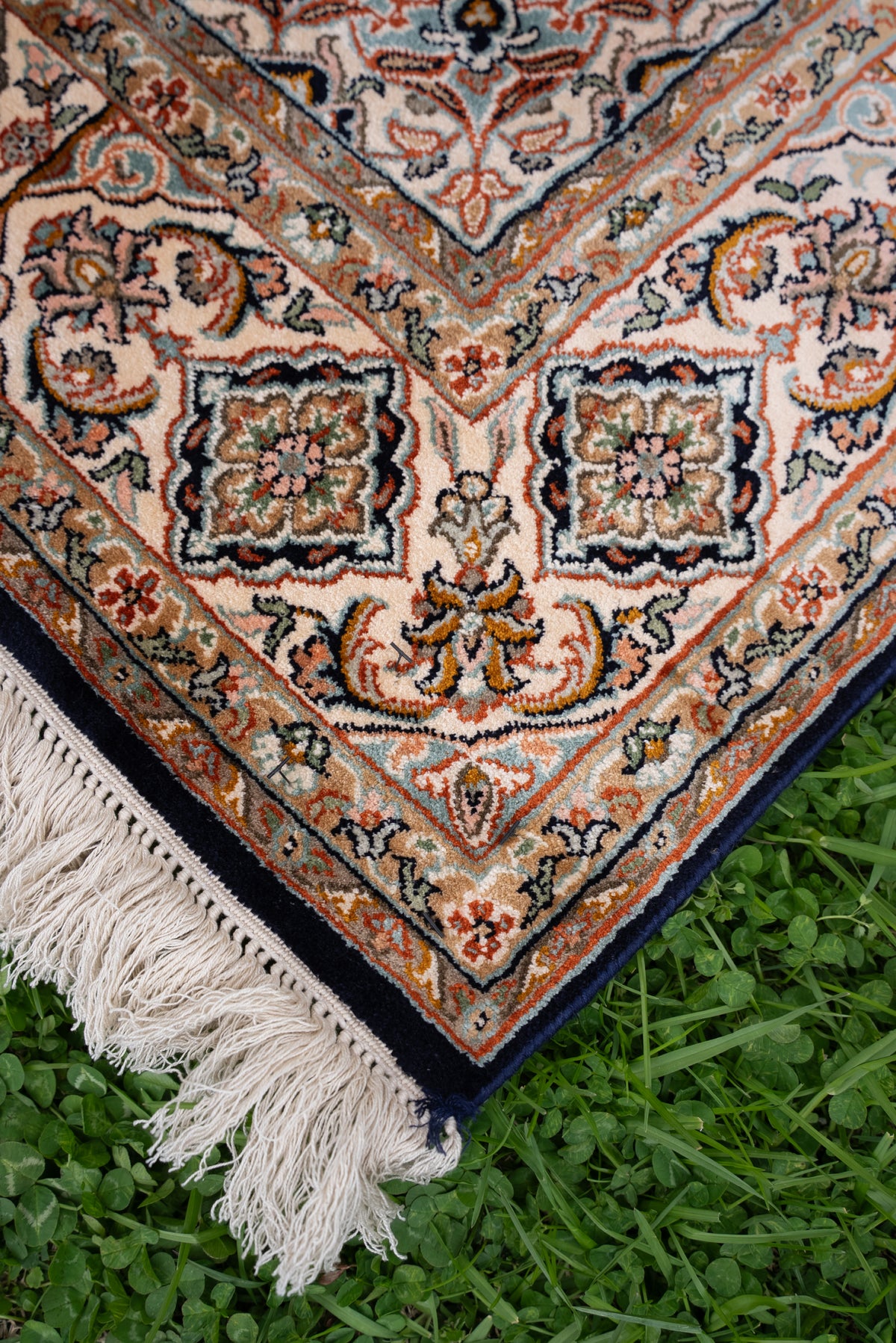 Angled corner of a mulberry silk carpet with cream floral borders, rust and green details, dark edging and ivory fringe