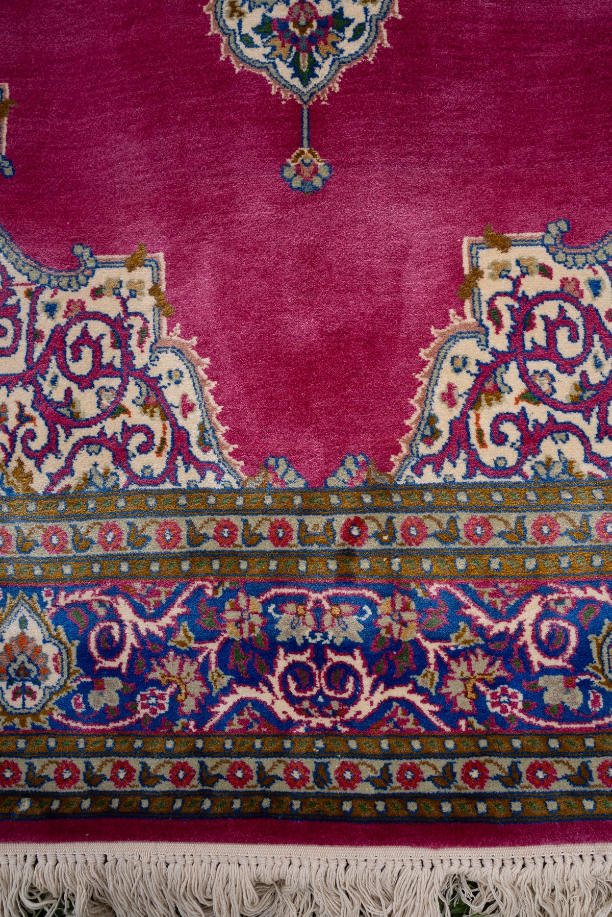 Lower rose-pink carpet field with ornate cream corners above blue floral borders and ivory fringe