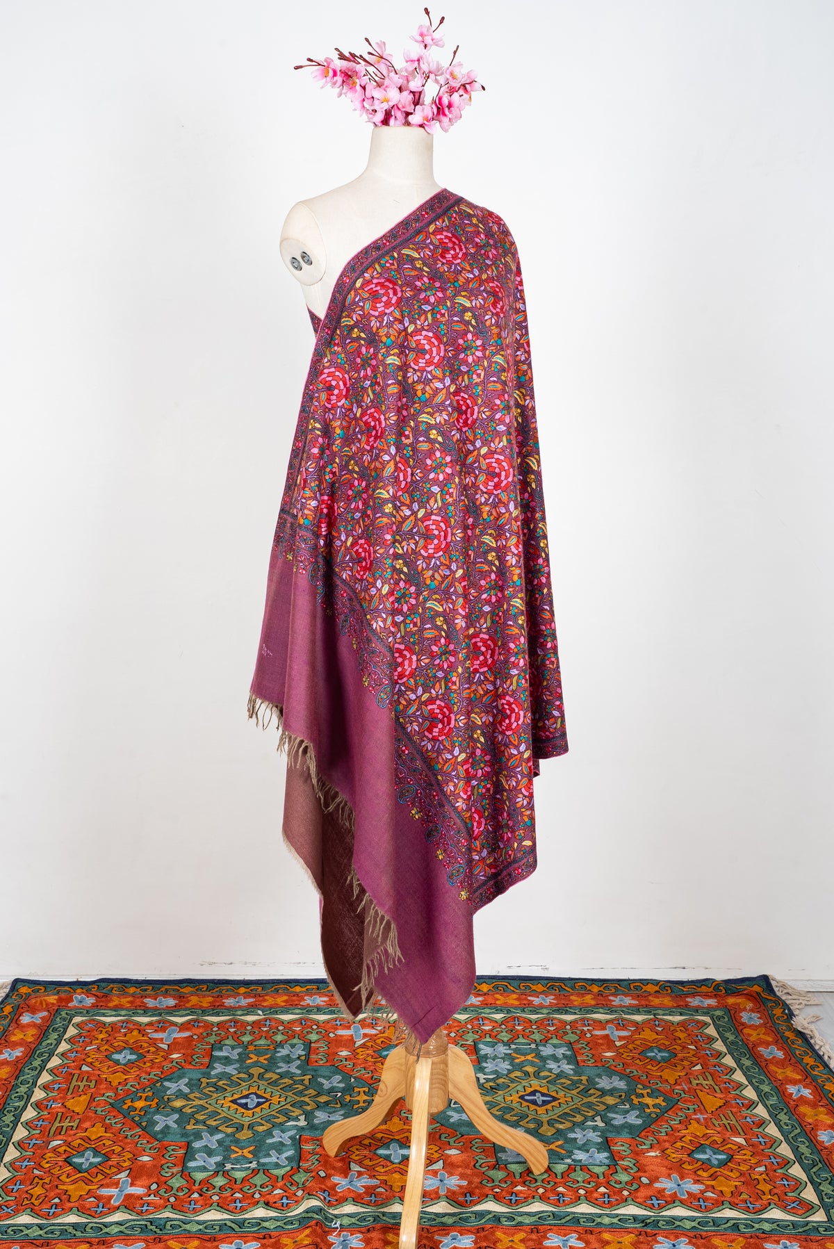 Full-length view of a plum Pashmina shawl on a mannequin, with multicoloured floral embroidery and a broad plain fringed end