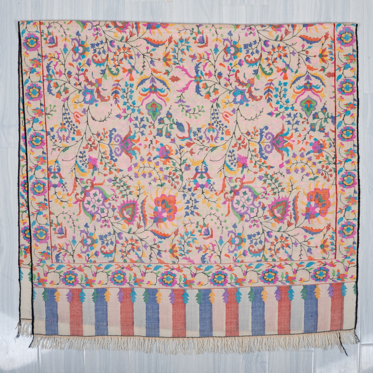 Ivory Pashmina shawl spread flat, with multicoloured floral motifs, matching borders and blue and pink striped ends