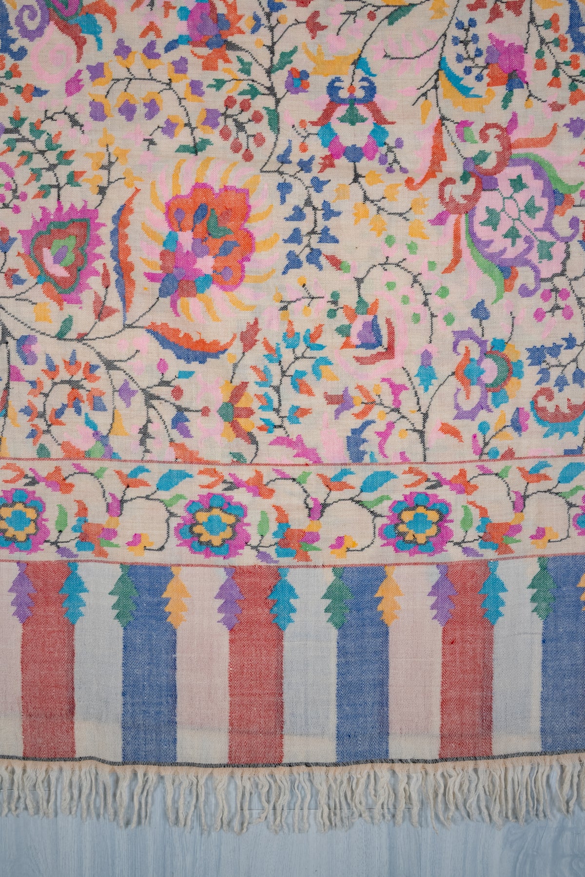 Ivory Pashmina shawl end detail showing colourful floral motifs above the matching border and blue and pink stripes