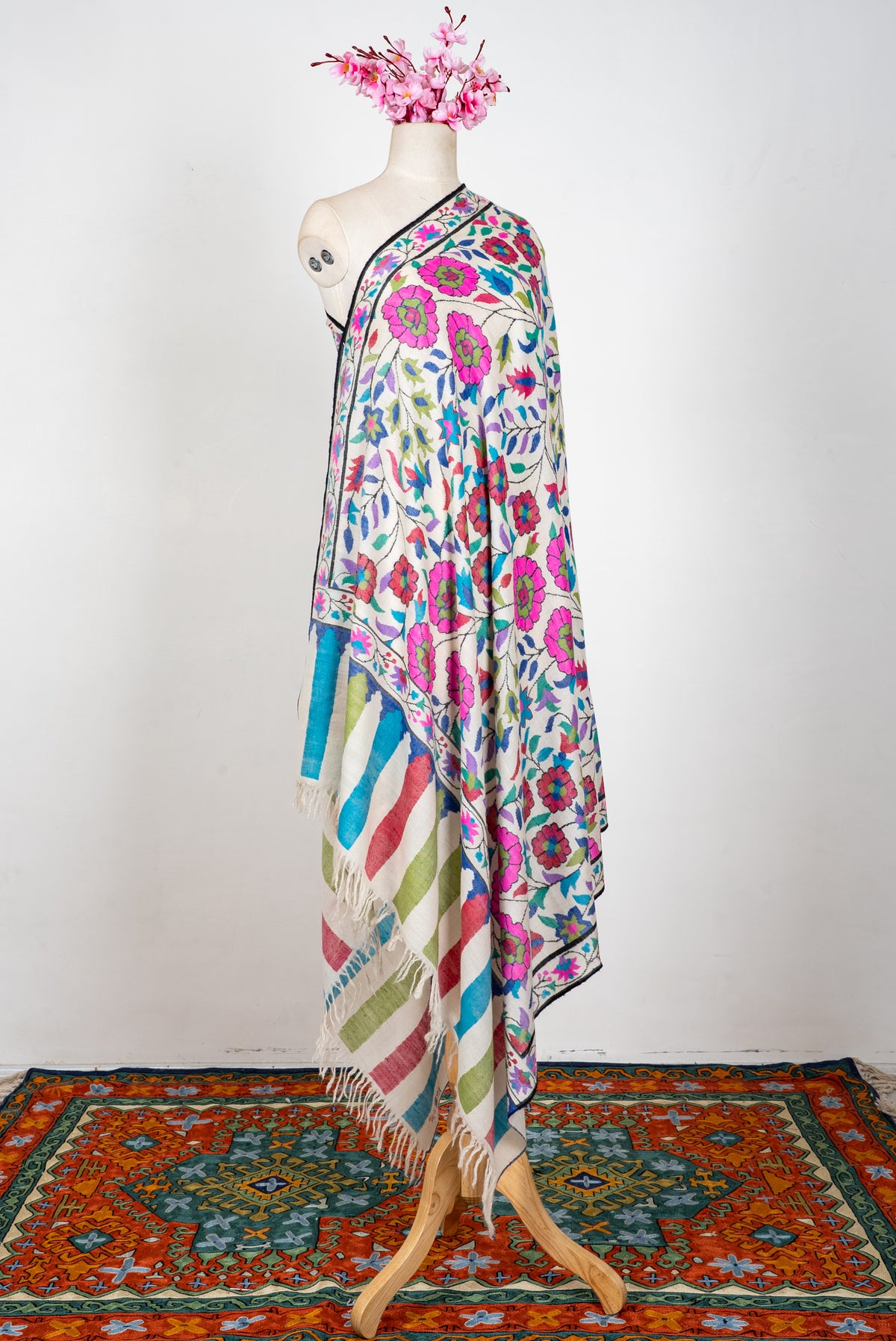 Side view of an ivory Pashmina shawl on a mannequin, with colourful floral vines and red, green and turquoise striped ends