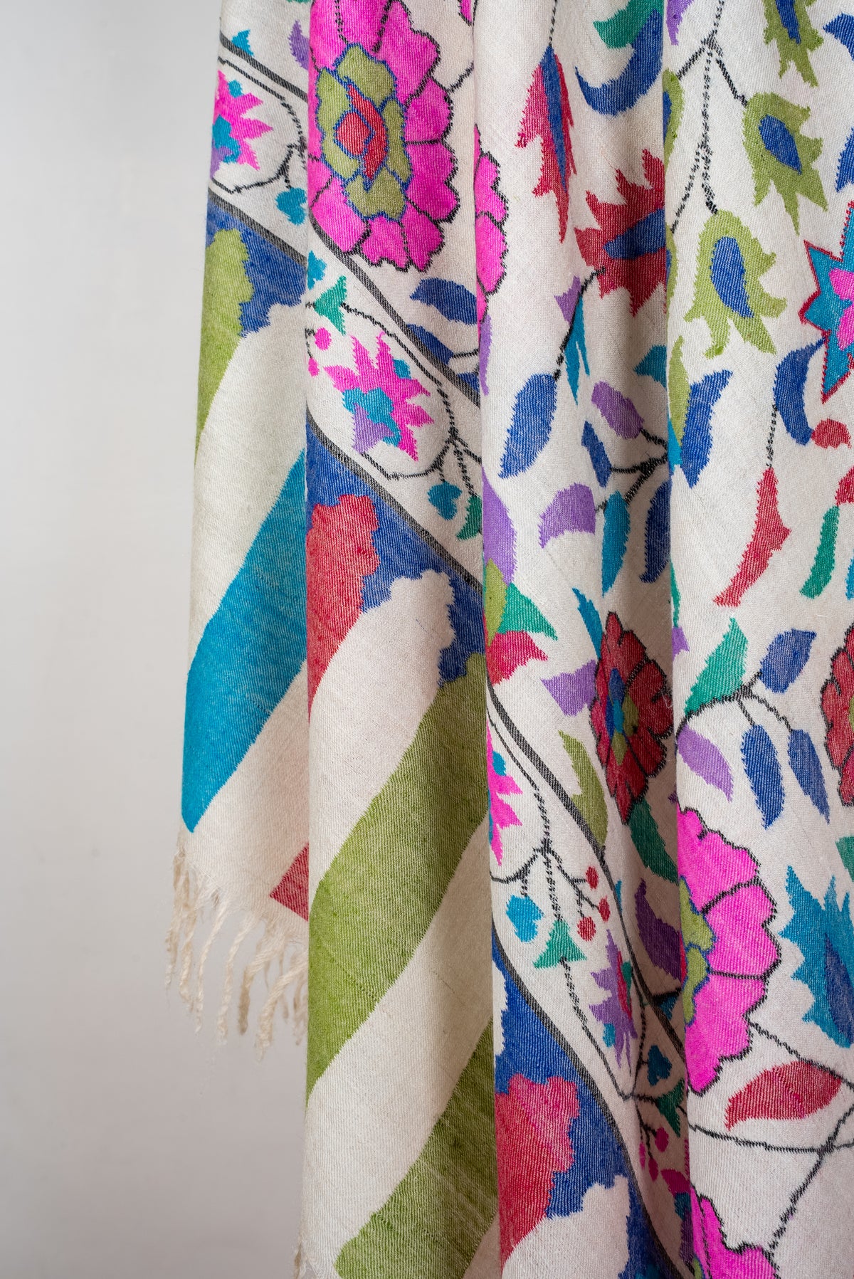 Colourful floral folds of an ivory Pashmina shawl with red, green and turquoise end stripes and cream fringe