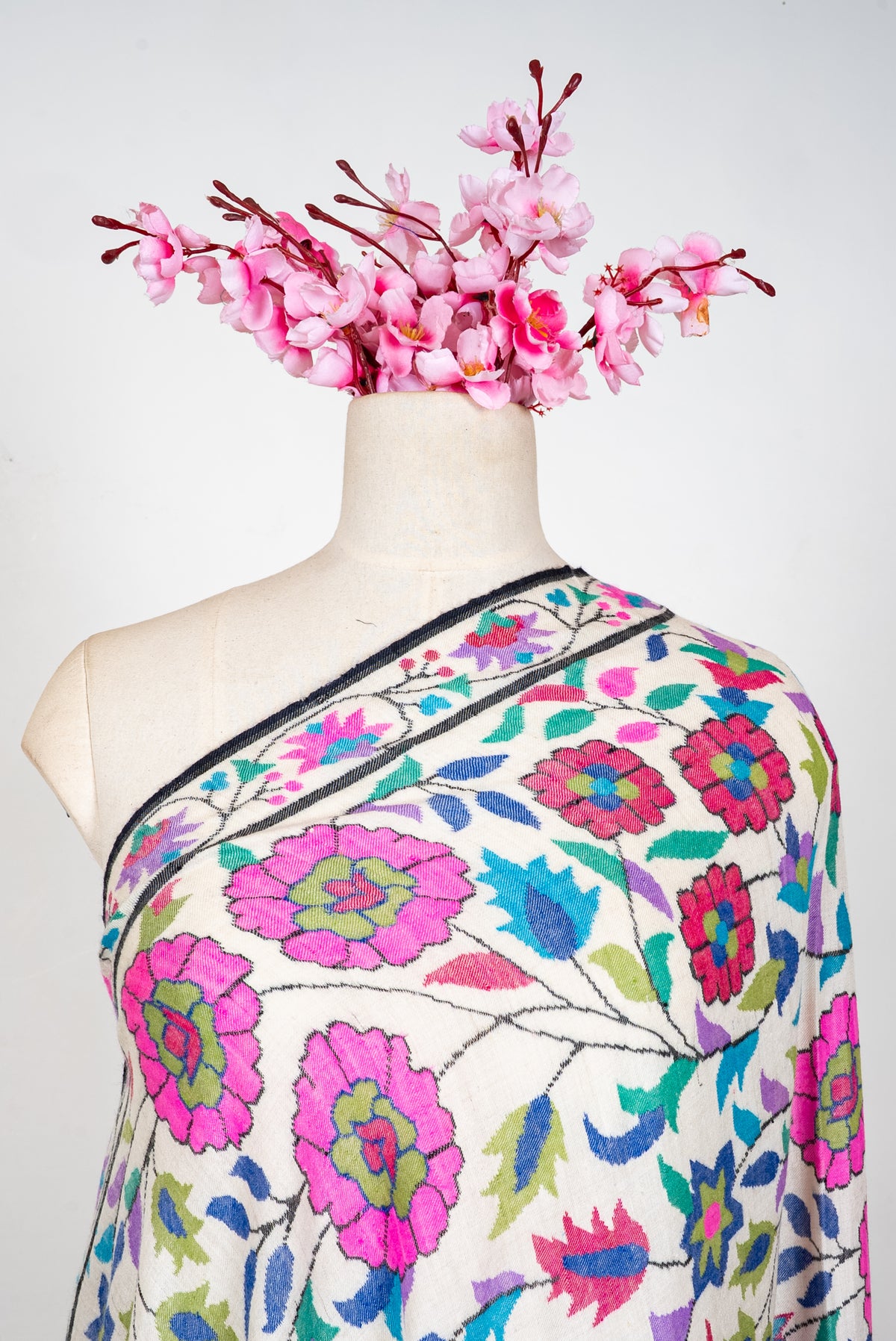 Ivory Pashmina shawl across a mannequin's shoulder, with bright pink flowers and colourful leafy vines