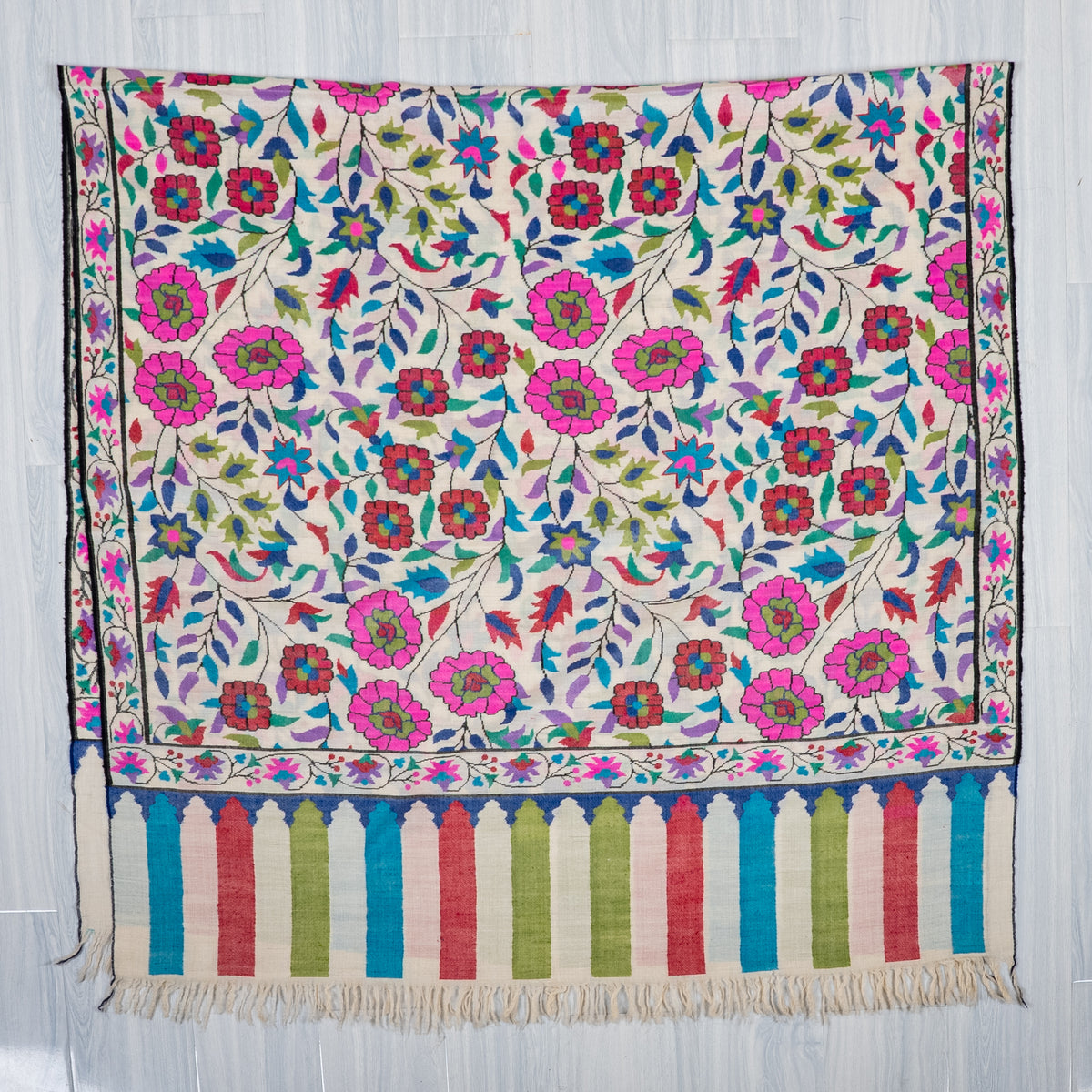 Ivory Pashmina shawl laid flat, with bright floral vines, a narrow flower border and multicolour striped fringed end