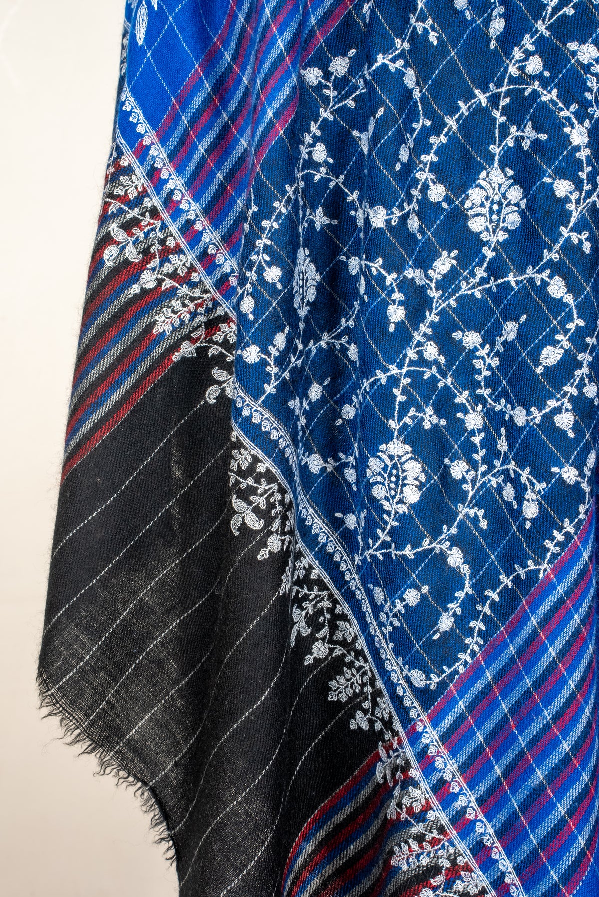 Close-up of Pashmina shawl folds with white floral vines, blue and red stripes and a dark finely striped fringed end
