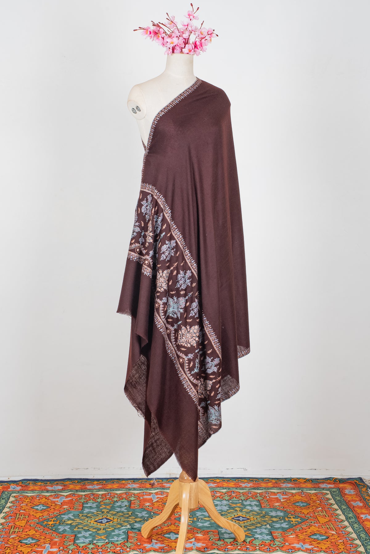 Chocolate-brown Pashmina shawl draped on a mannequin, with fine embroidered sides and a pastel floral panel near the end.