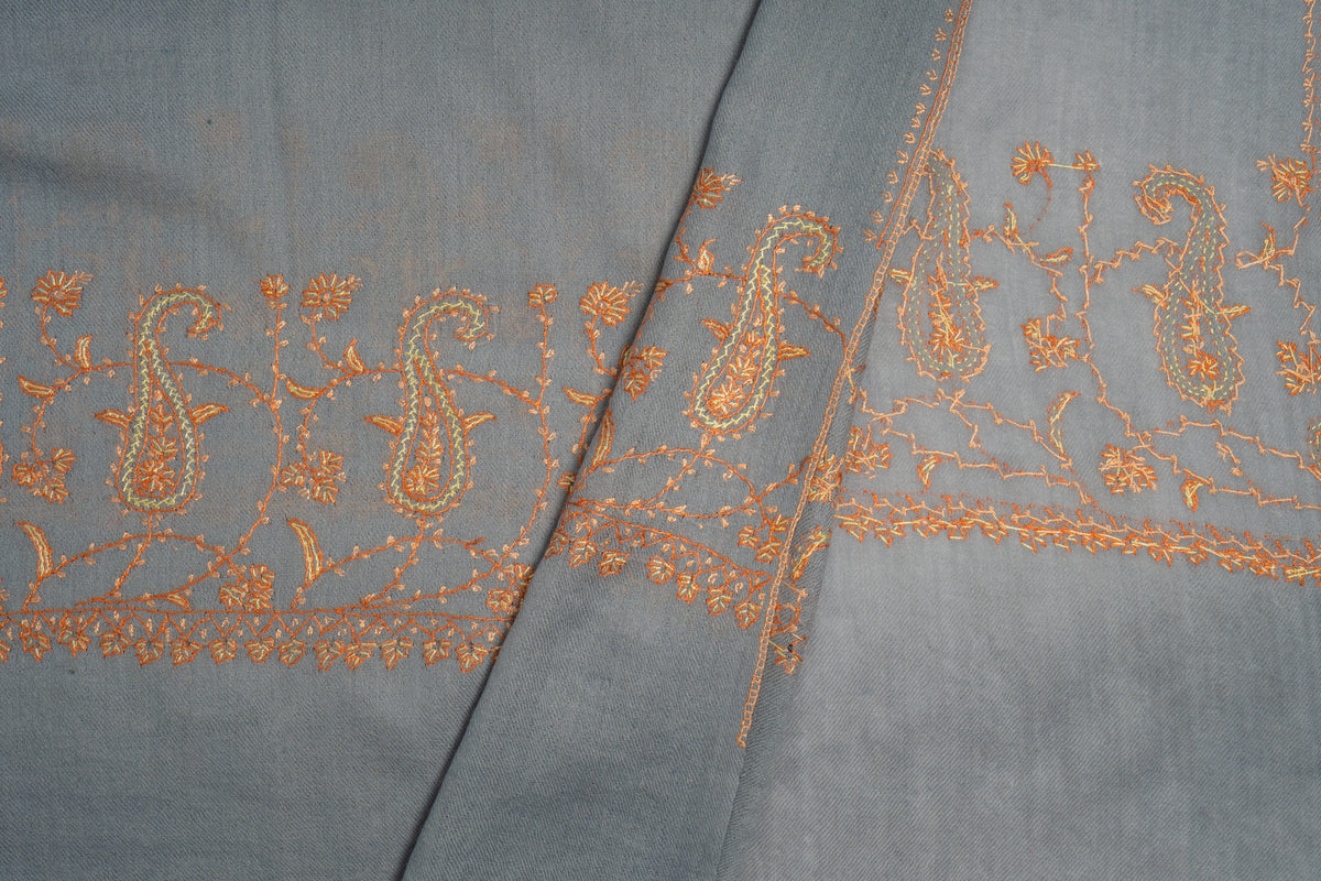 Folded grey stole ends showing delicate orange paisley and floral embroidery beside narrow stitched edges.