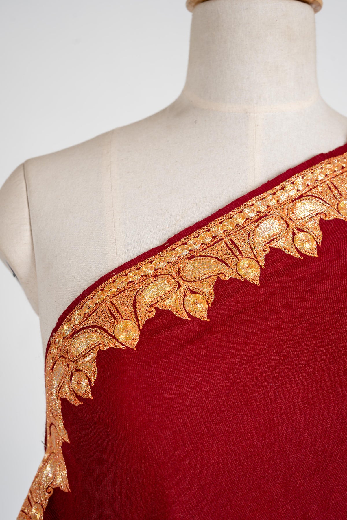 Close-up of the crimson shawl shoulder edge with gold-coloured paired leaves and pointed buds.