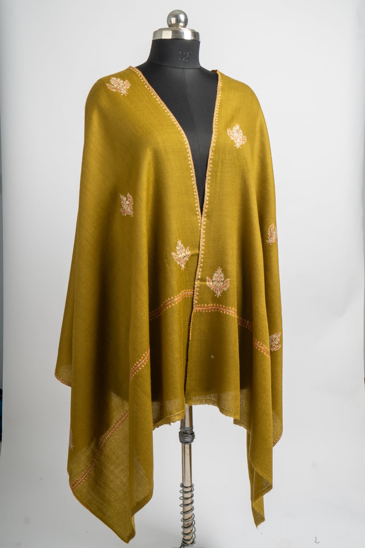 Olive-green merino wool stole draped open on a mannequin, with scattered pale floral Sozni motifs and narrow embroidered borders.