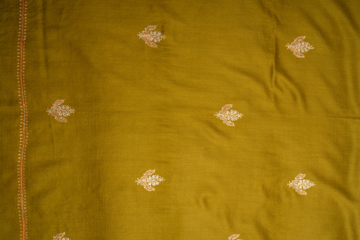 Flat detail of scattered pale floral sprigs across olive-green merino wool beside a fine embroidered side edge.