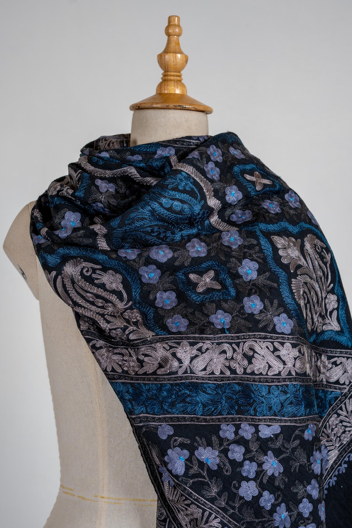 Close wrapped view of the black stole with small blue flowers and large silver-toned leafy motifs in bordered panels