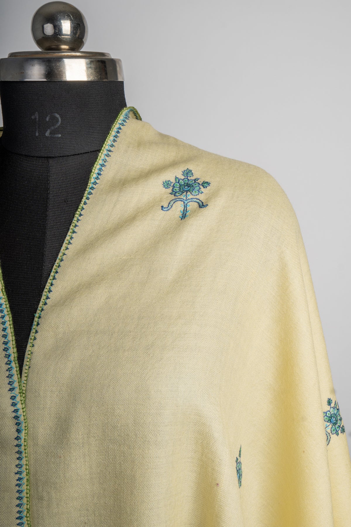 Shoulder detail of the buttercream stole with a teal flower sprig beside the fine embroidered edge.