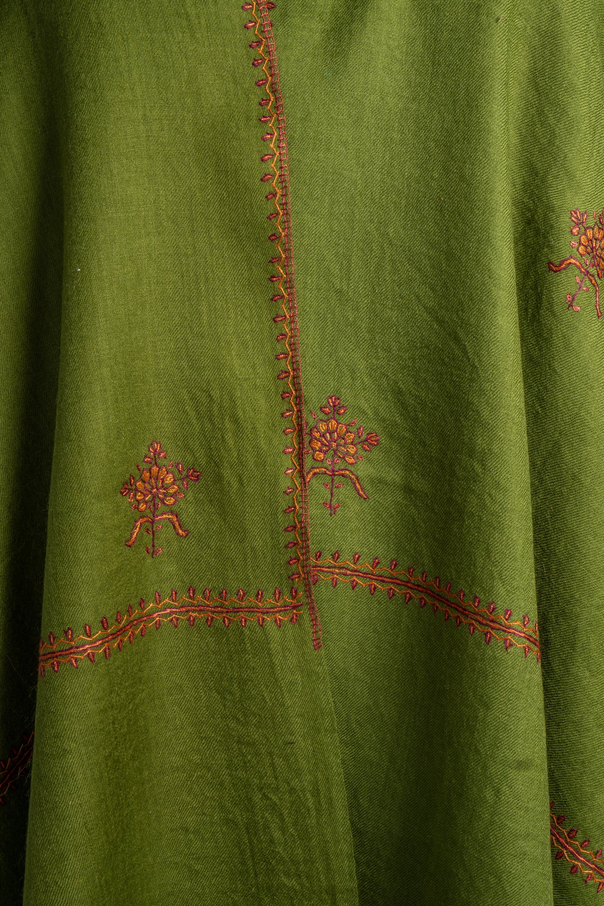 Front detail of a green Merino wool stole with small red and orange Sozni floral motifs beside intersecting borders