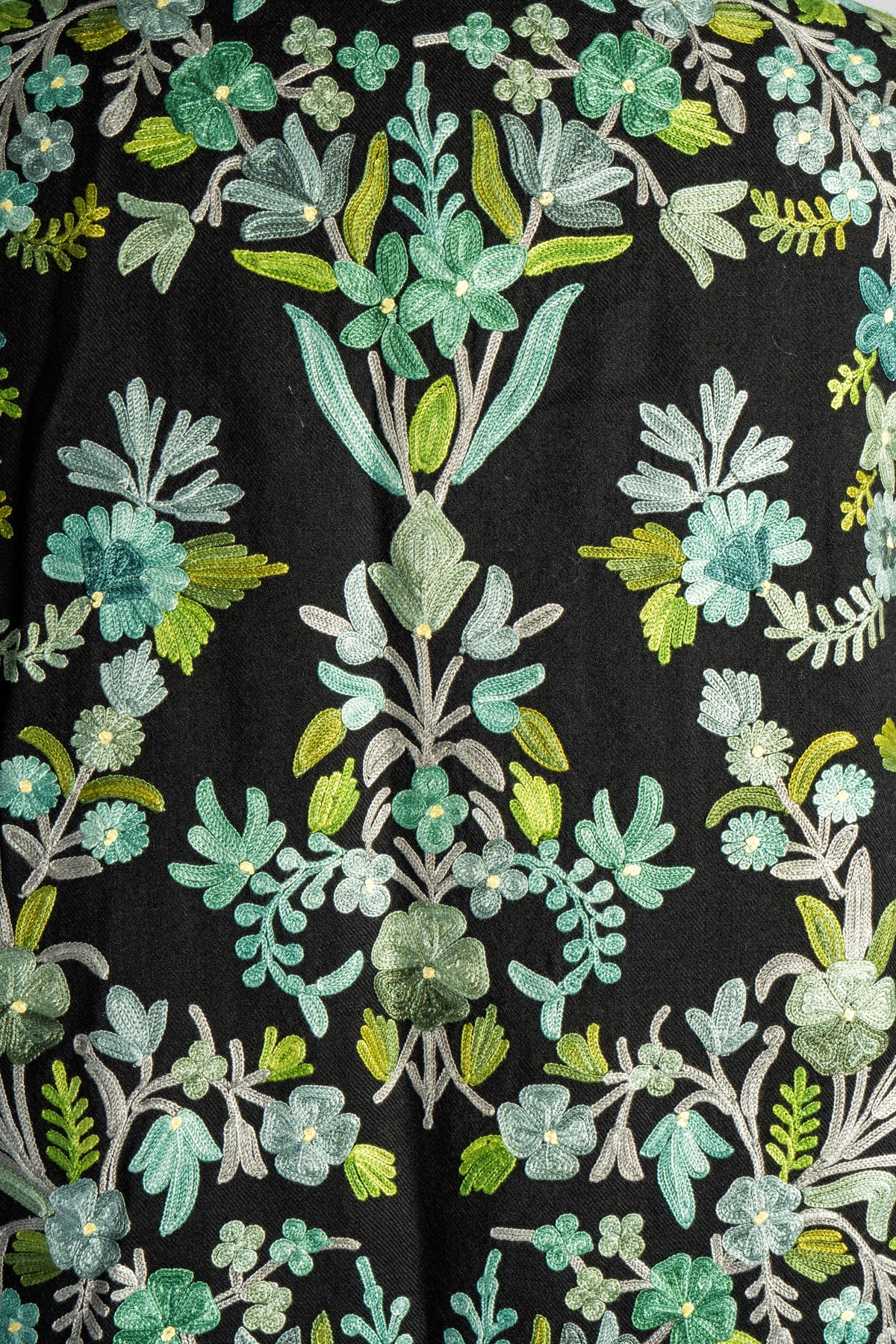 Close-up of mint flowers, pale stems and bright green leaves forming branching Aari vines across the black jacket’s back.