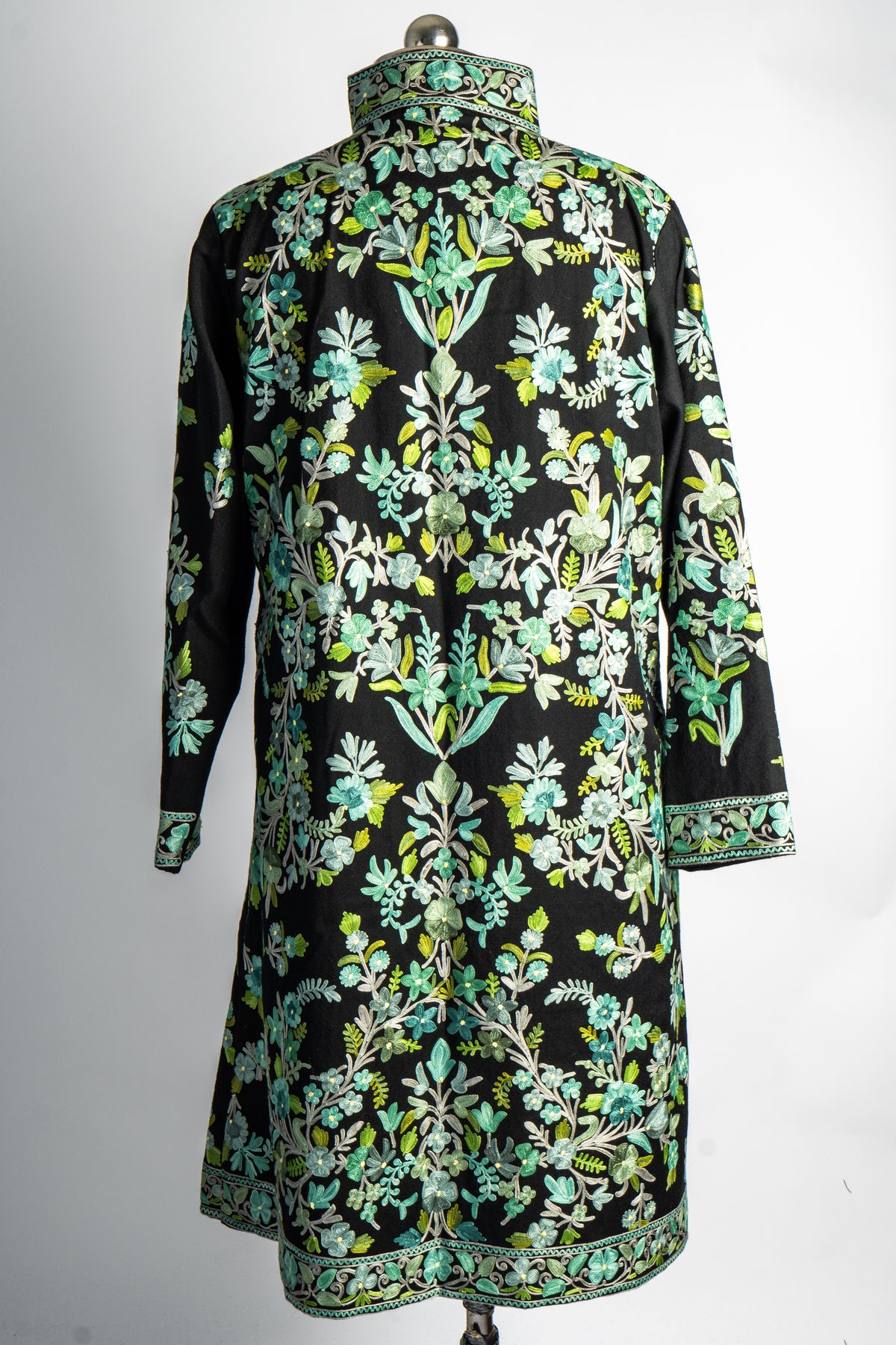 Back of the black long jacket covered with mint and green floral vines, with embroidered borders at the collar, cuffs and hem.