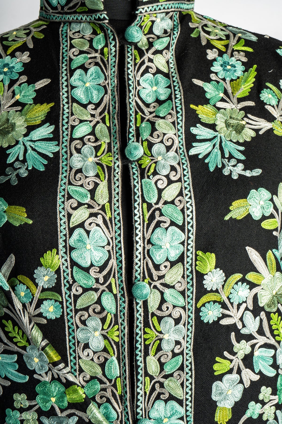 Detail of the black jacket’s buttoned opening, edged with mint flowers, curling stems and pale green leaves.