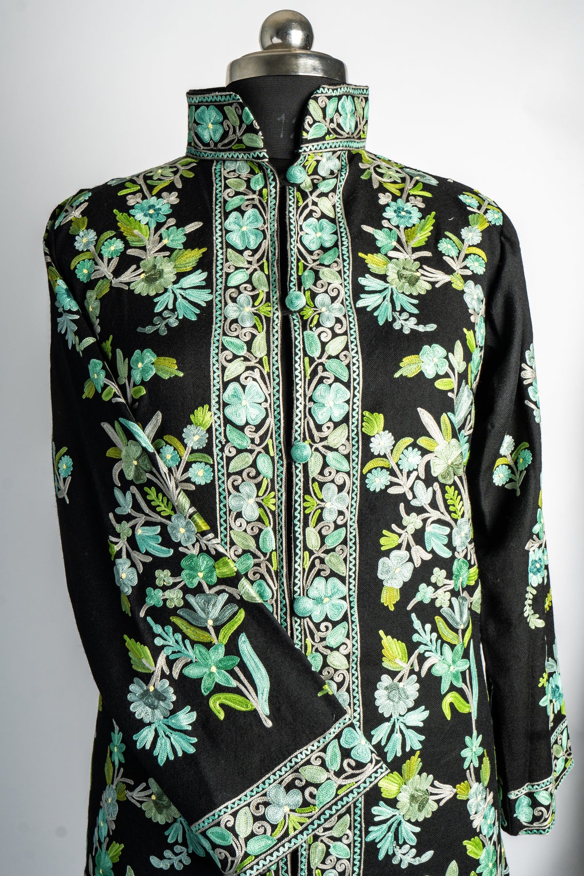 Upper front of the black jacket with mint floral embroidery, a stand collar and a folded sleeve edged with a matching border.
