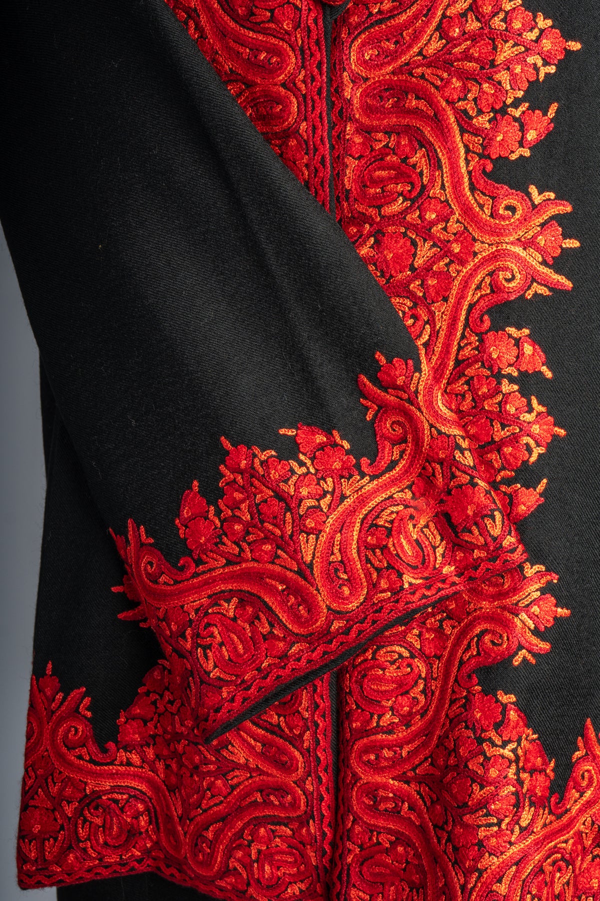 Crossed black jacket sleeve with a vivid red Aari paisley cuff over matching embroidered front and hem borders