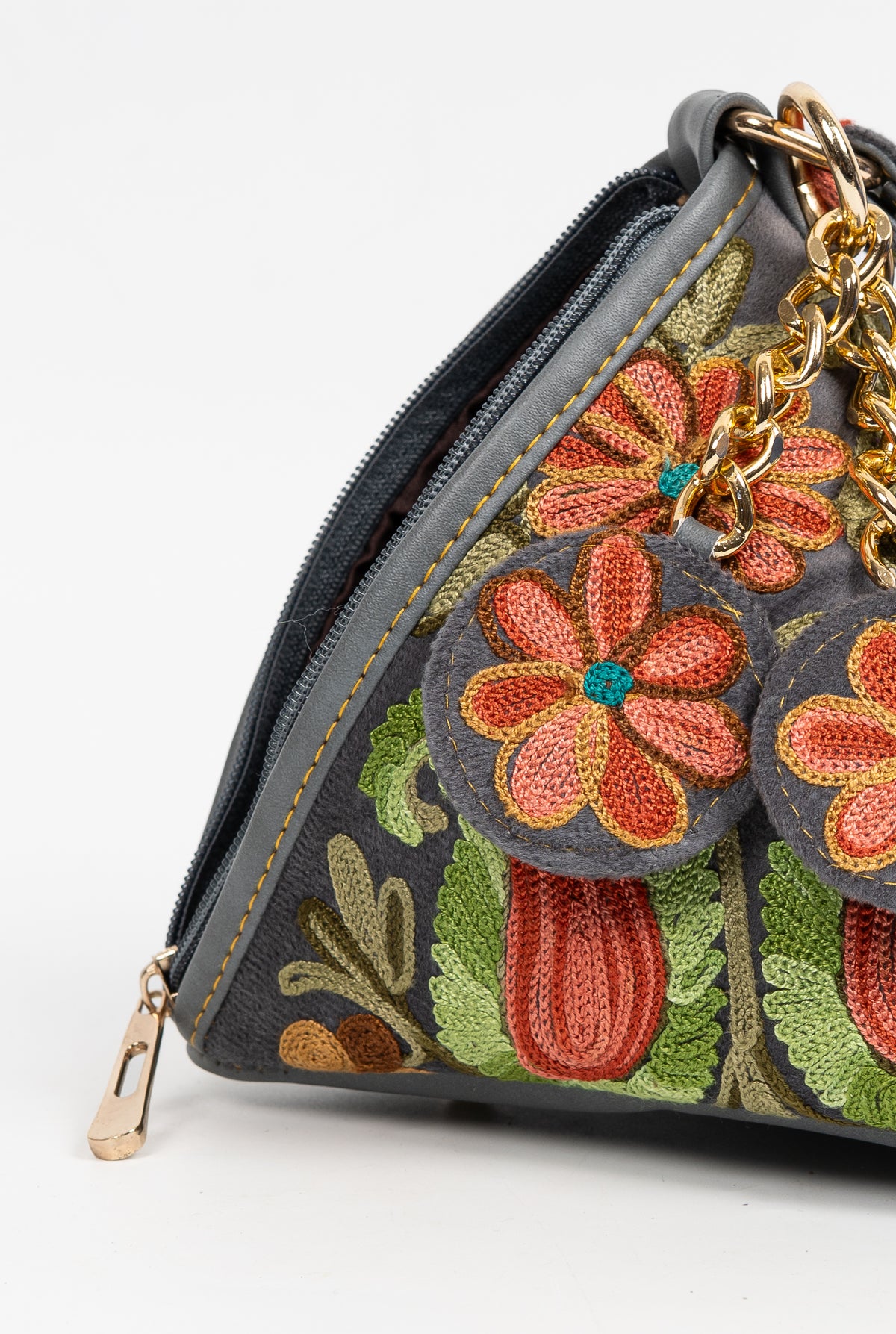 Detail of coral embroidered flower charms and gold-toned chain links against the pyramid bag’s paisley-patterned side